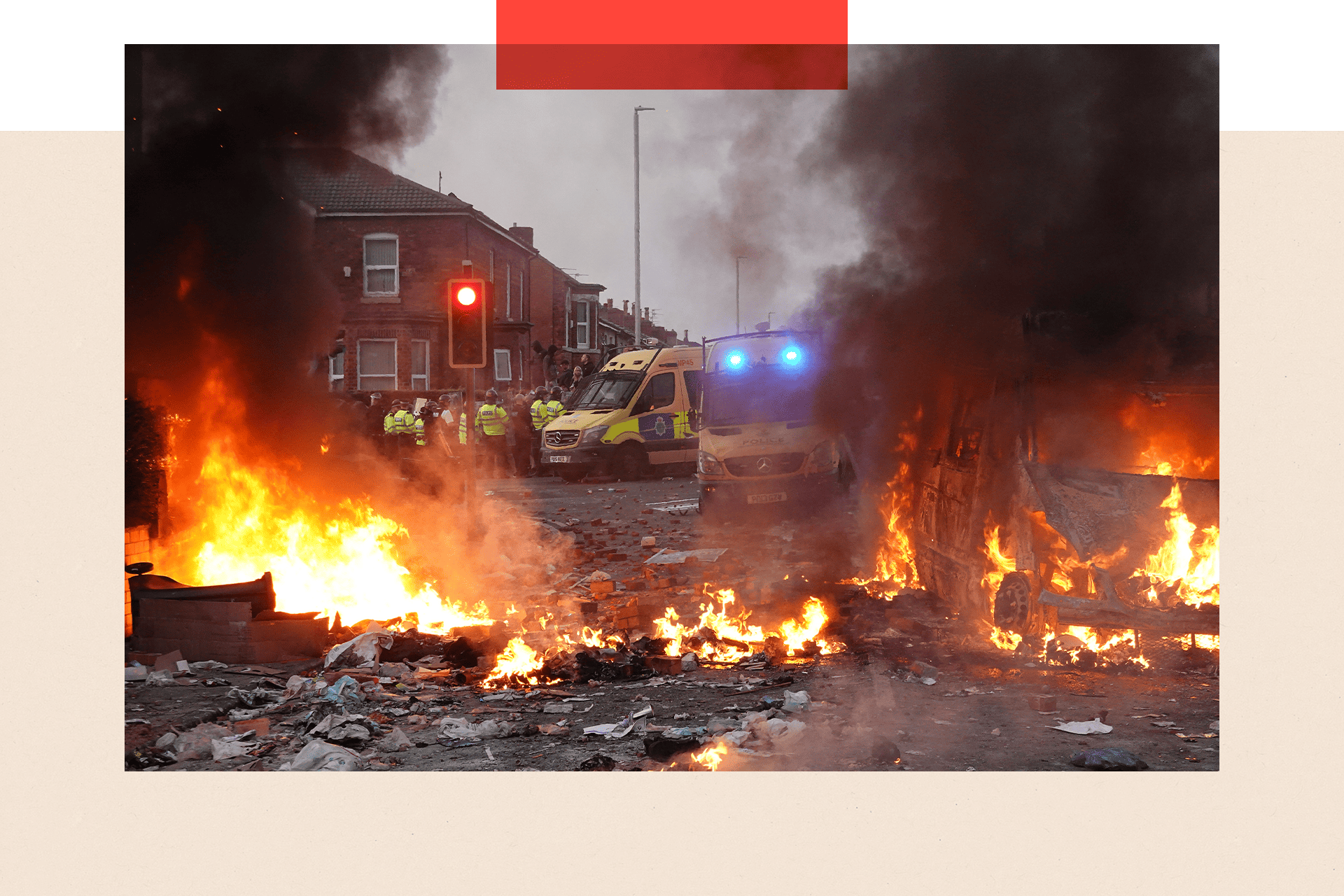 Colour image of riot police holding back protesters. In the foreground a police vehicle is engulfed by fire.