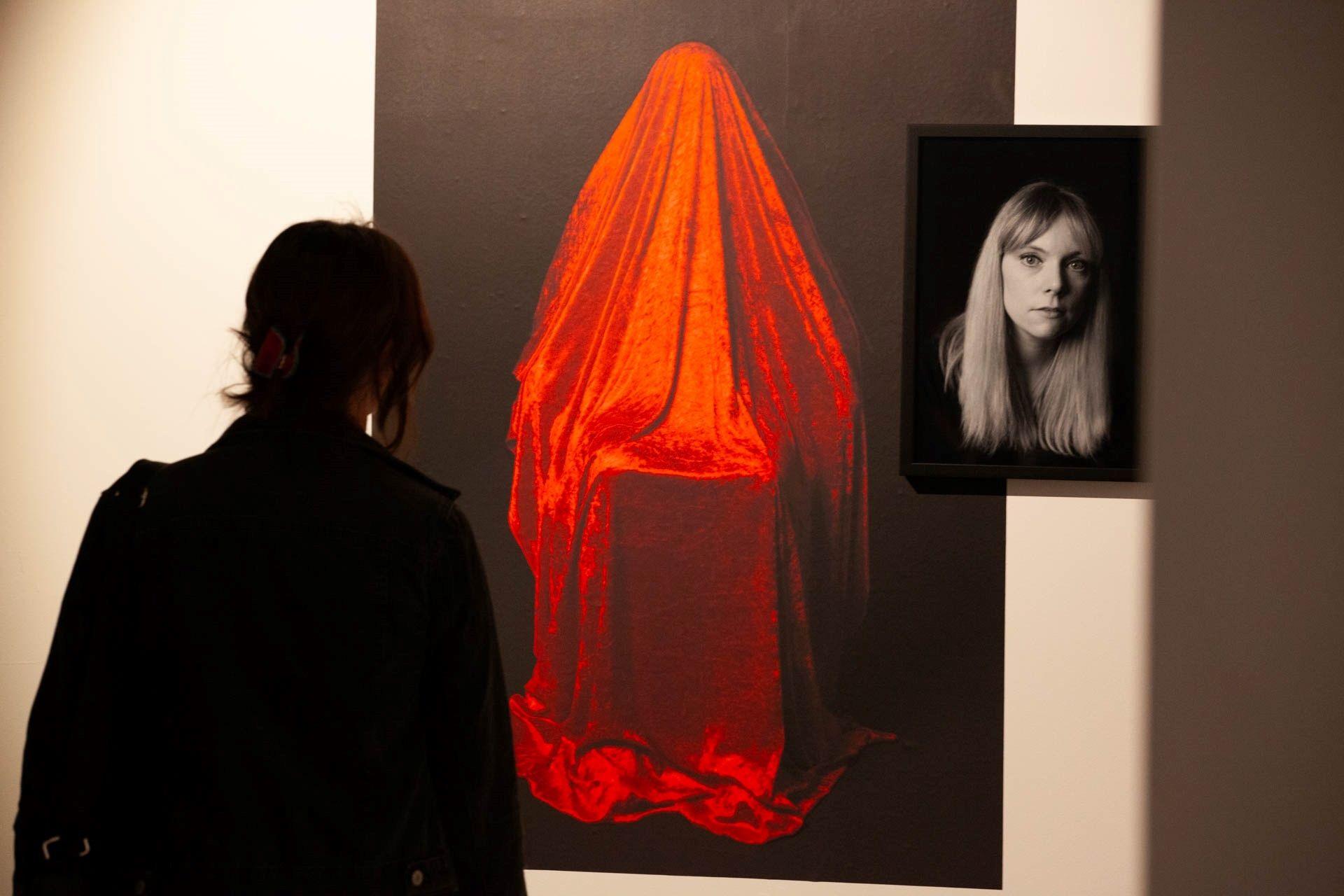 A woman looks on at a red Hidden Mothers image and black-and-white portrait side by side