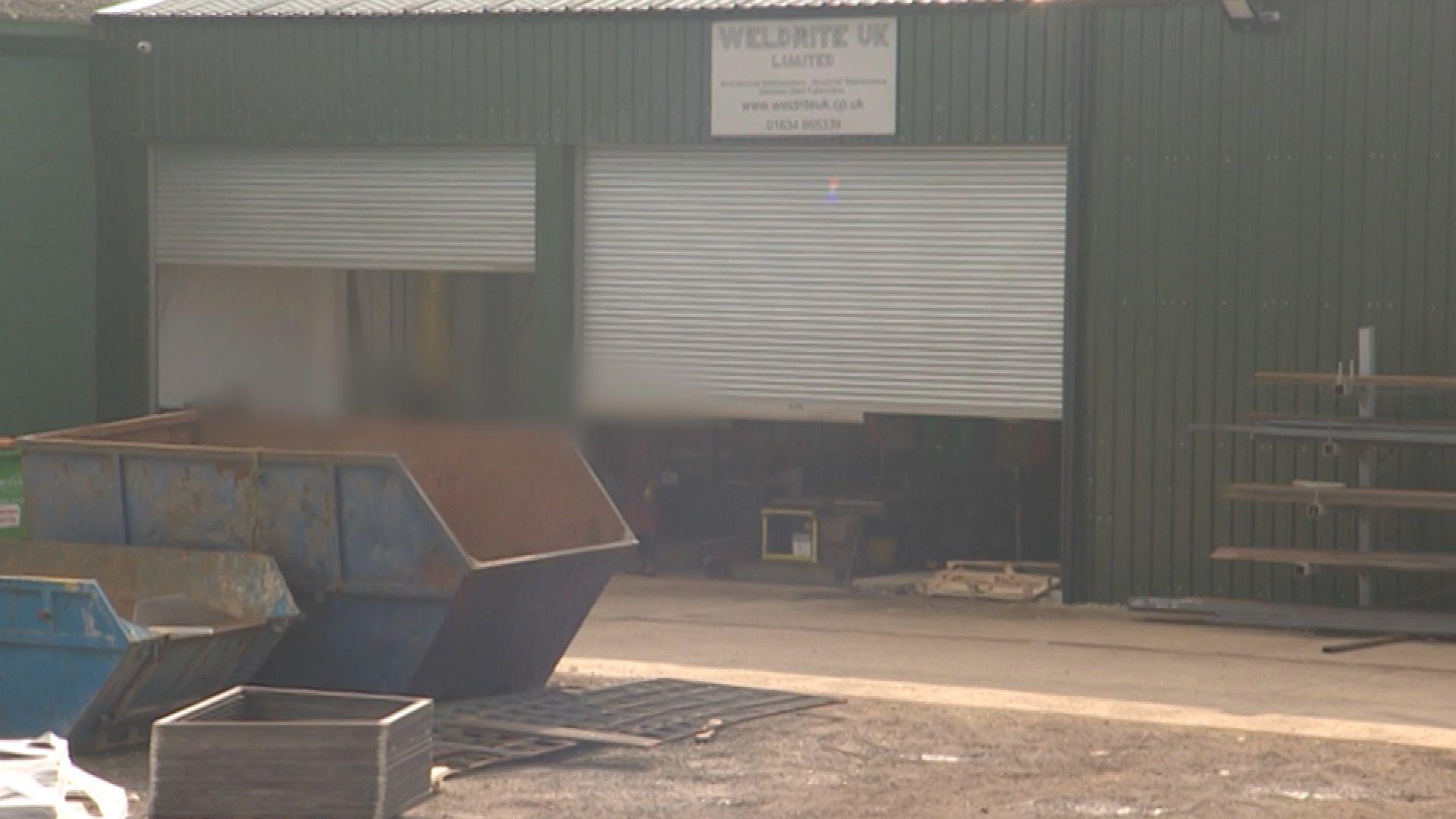 Exterior view of Weldrite UK factory building with roller doors and industrial skips outside.