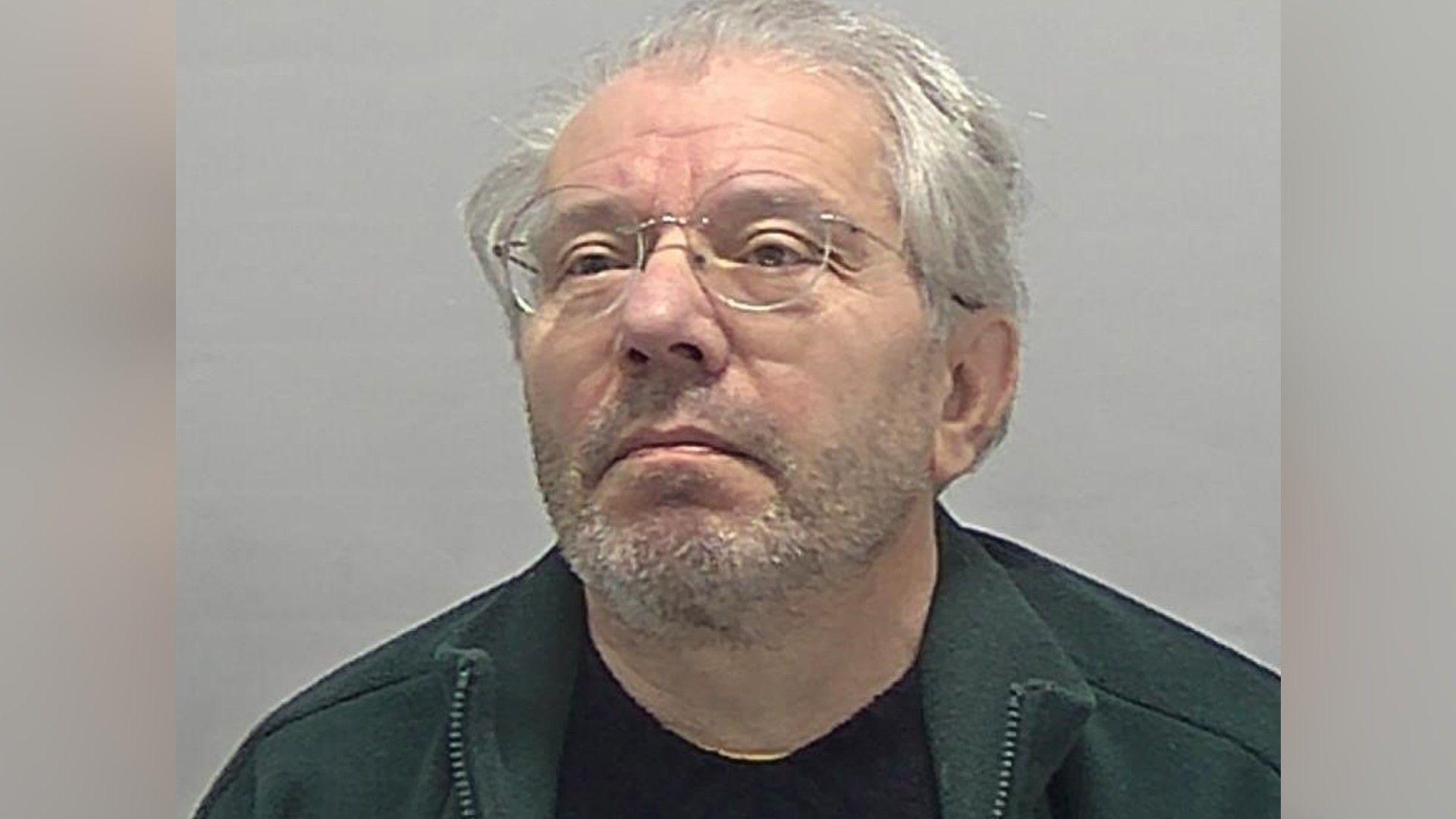 David Marriott wearing a green zipped fleece and a black T-shirt and round-rimmed glasses.