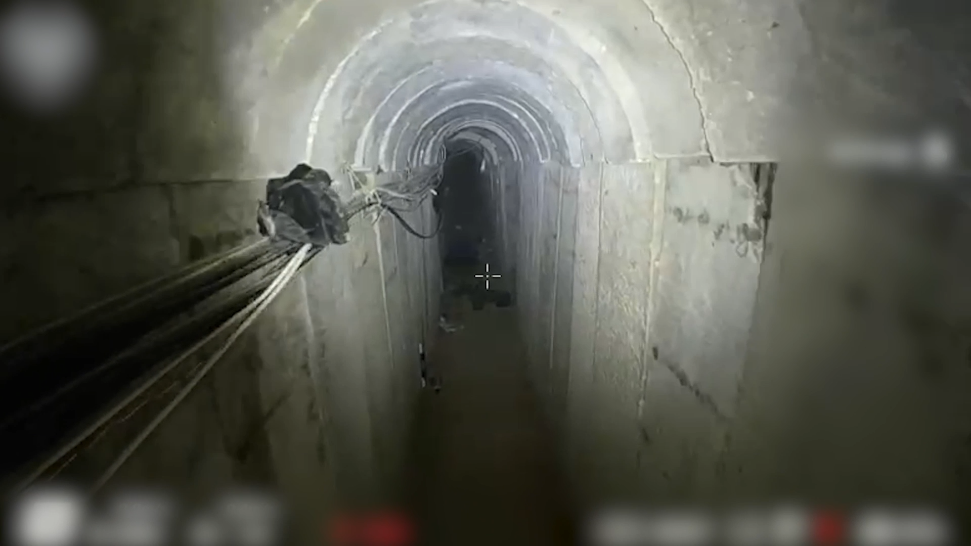 A still taken from footage of an underground tunnel structure. Wires can be seen running along the concrete slab walls, with items of clothing in the background.