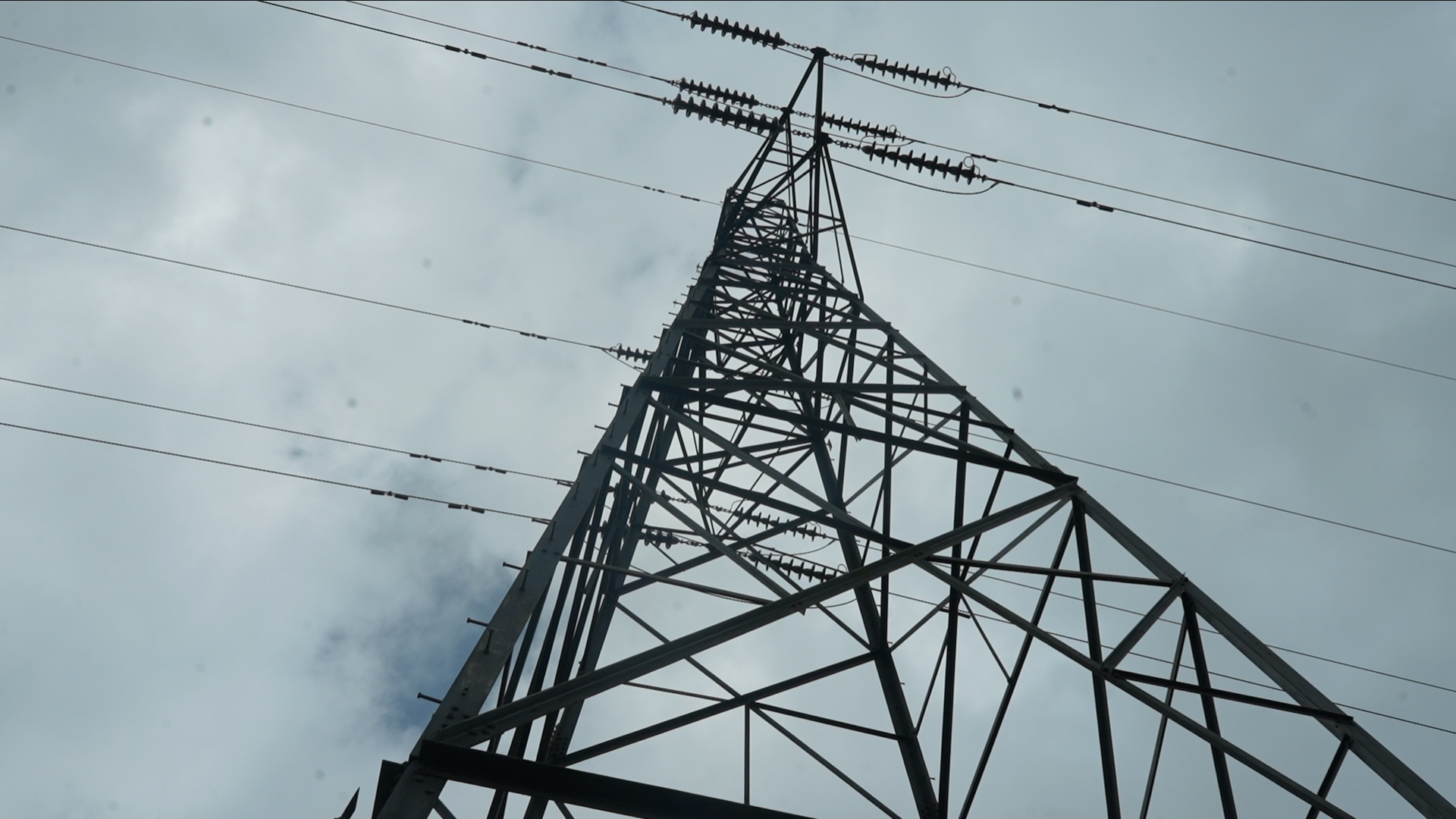 A general view of an electricity pylon. The view is from below the pylon looking up toward it. Cables can be seen coming horizontally away from it and there are grey clouds in the sky.