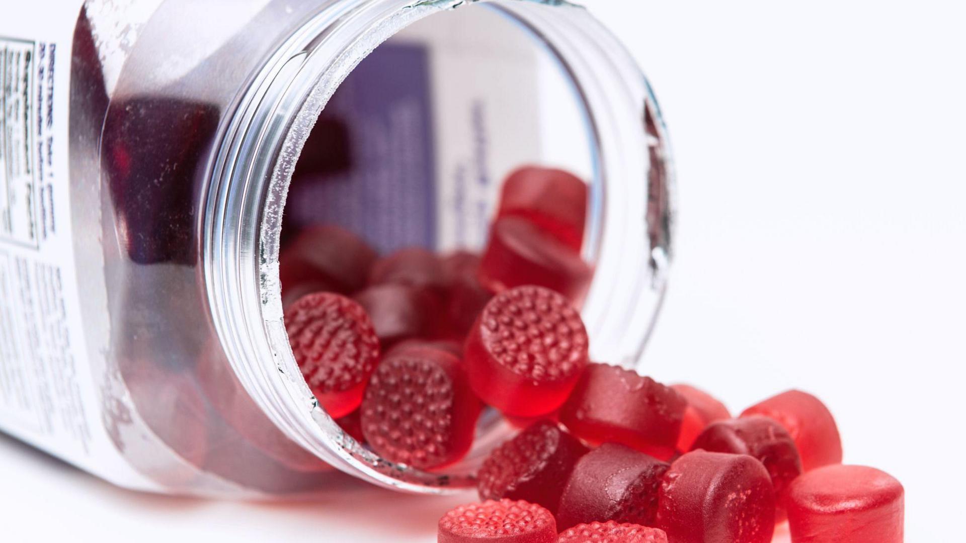 Unbranded red gummies falling out of an upended clear jar container
