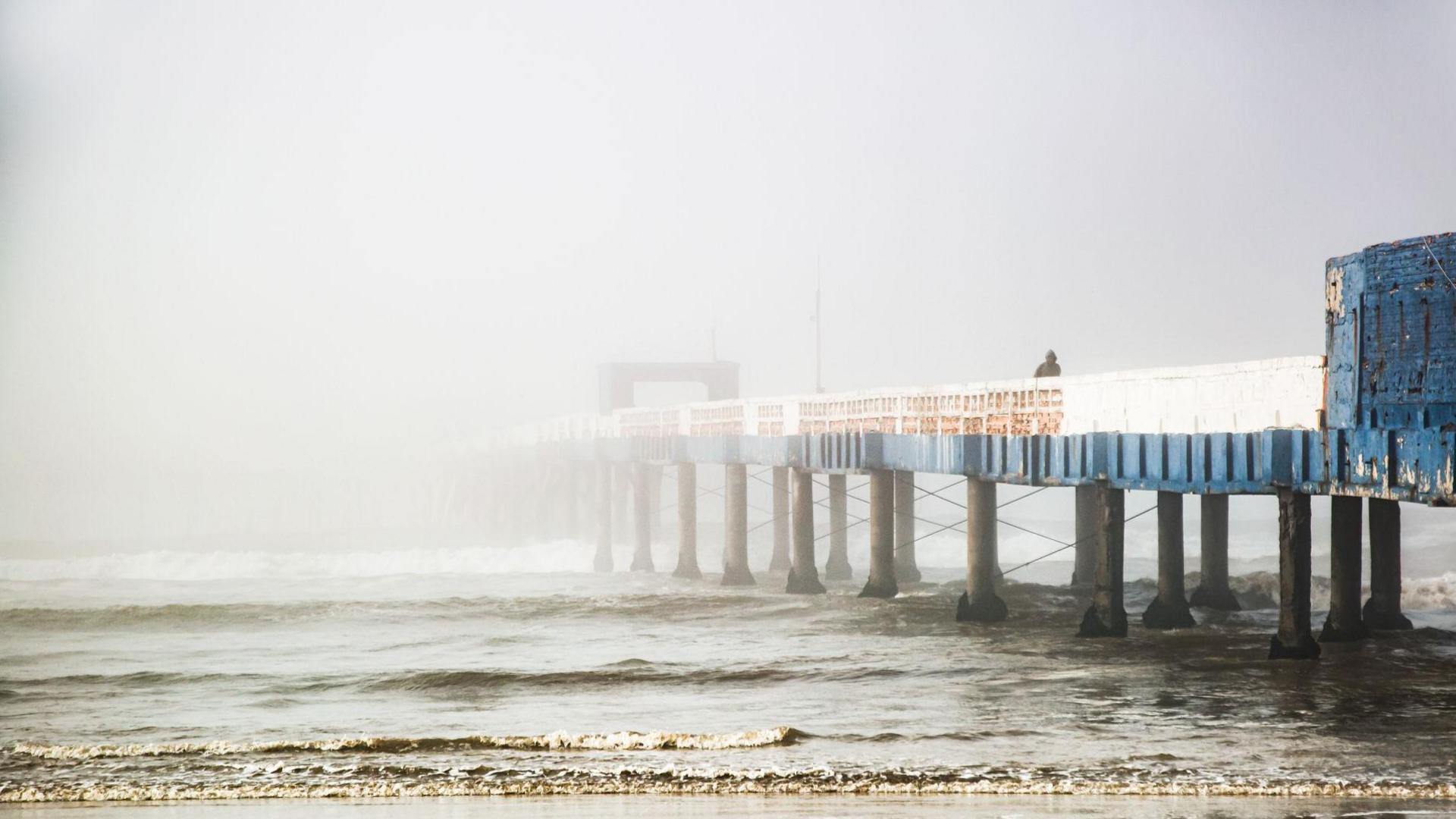 Image shows a pier disappearing into sea fog