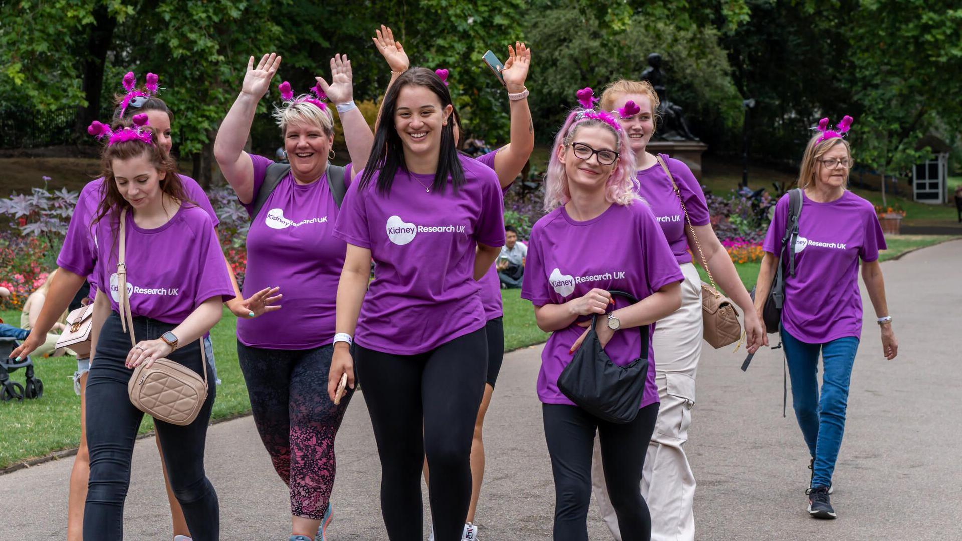 Seven people wearing purple Kidney Research UK t-shirts walking along a path. Two are holding up their arms.