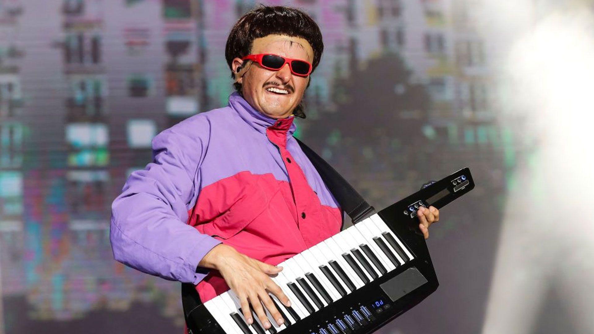 Picture of Oliver Tree in a purple and pink jacket performing in 2024. He is holding a keyboard.