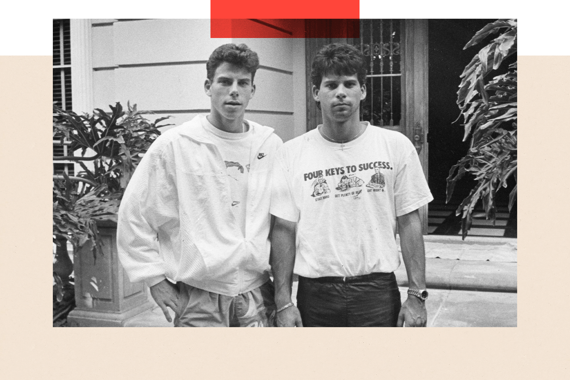 The Menendez brothers, Erik on the left and Lyle on the right, pose for a photo. Erik wears a graphic T-shirt partly covered by a light jacket, with one hand in his trouser pocket. Lyle sports a similar T-shirt, black trousers, and a watch on his right wrist. They stand in front of a gate