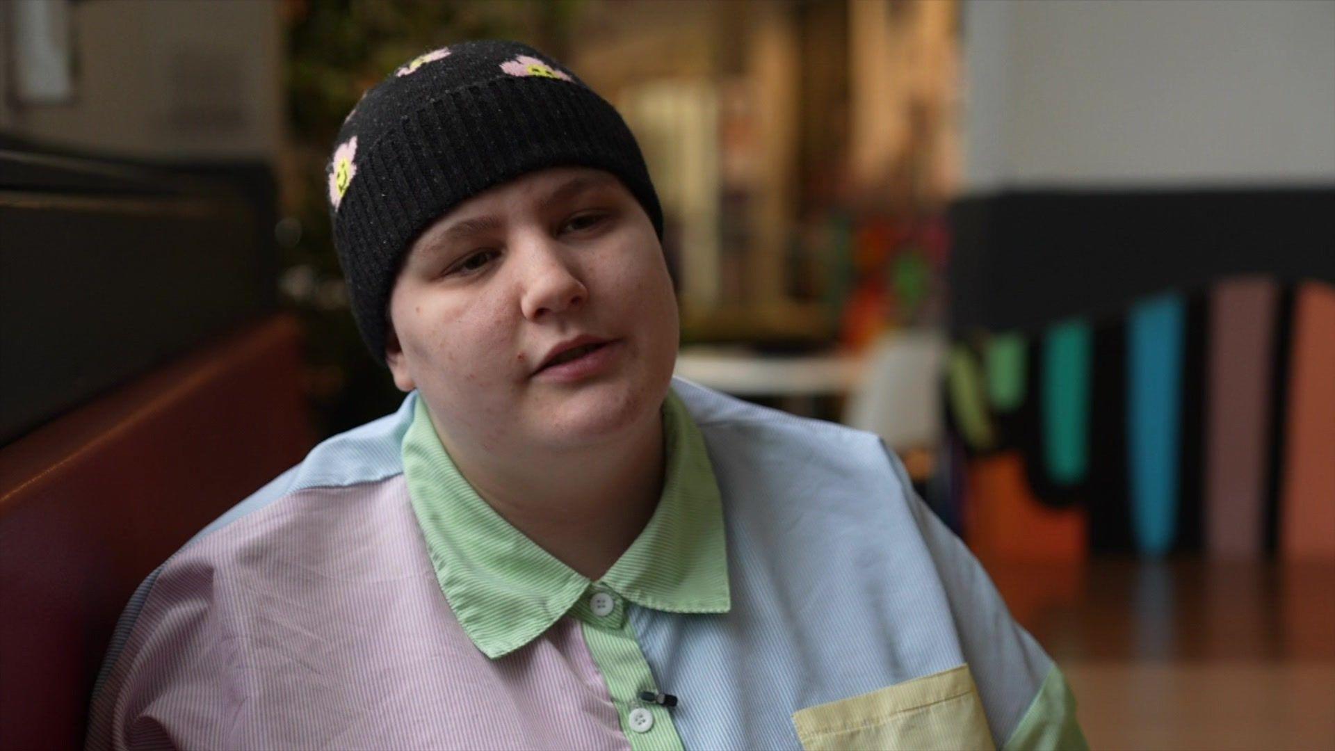 Rhyen smiling at the camera, wearing a black beanie hat and a multicoloured shirt