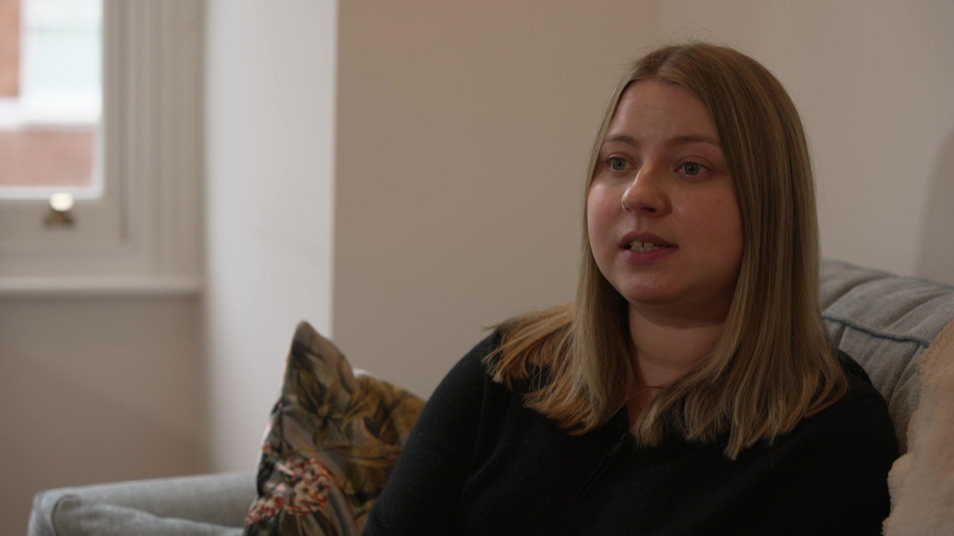 A women sits on a sofa in conversation with someone off camera