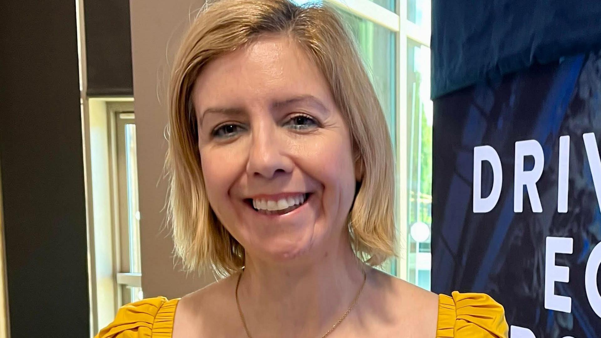 Greater Lincolnshire Mayor Dame Andrea Jenkyns pictured in front of a display board. She is wearing a mustard-coloured top and is smiling at the camera.