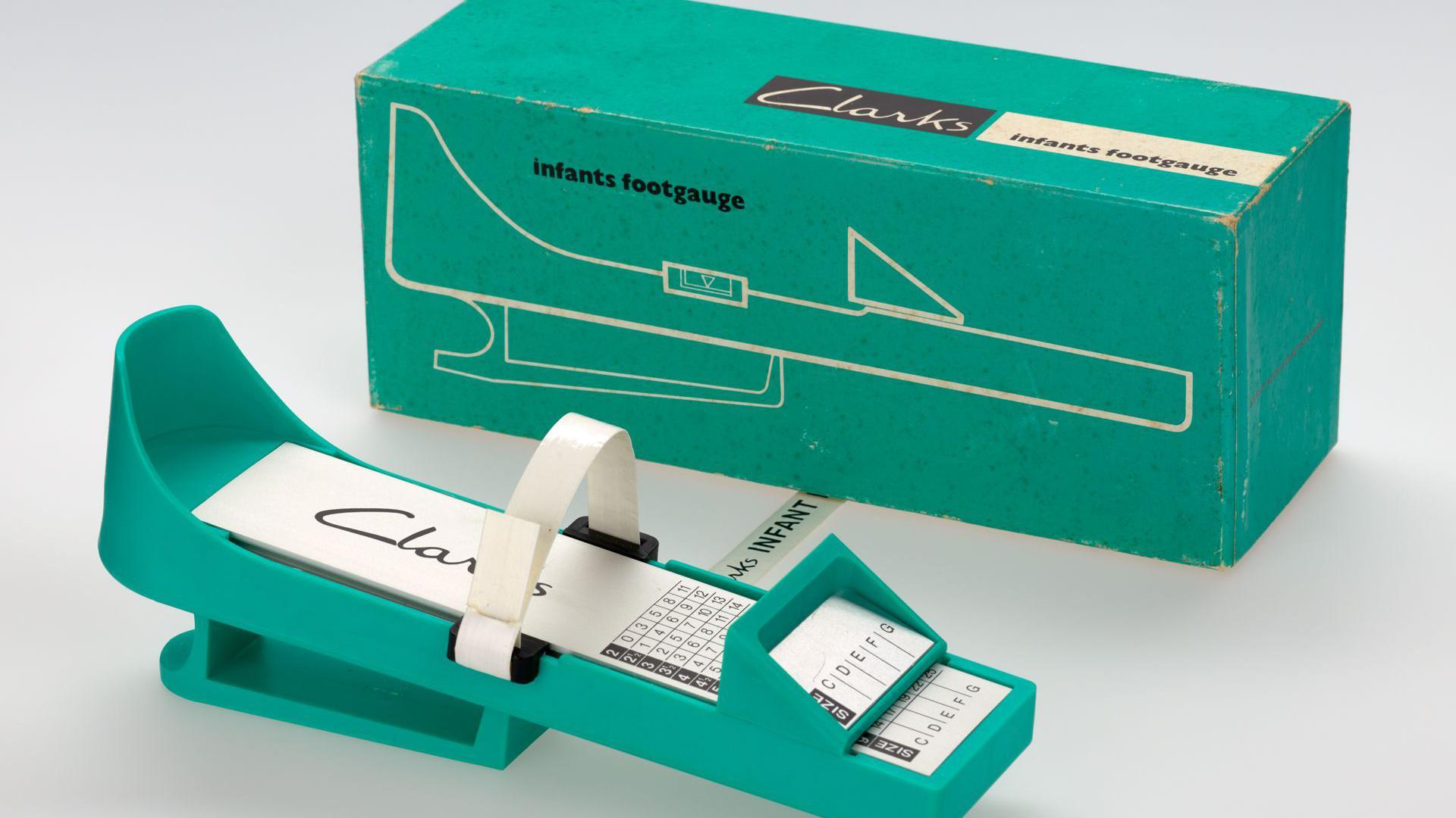 A device used to measure children's feet. It is made of green plastic and shaped like an insole, with a strap to fit around the foot. There are numbers and letters underneath where the toes would sit.