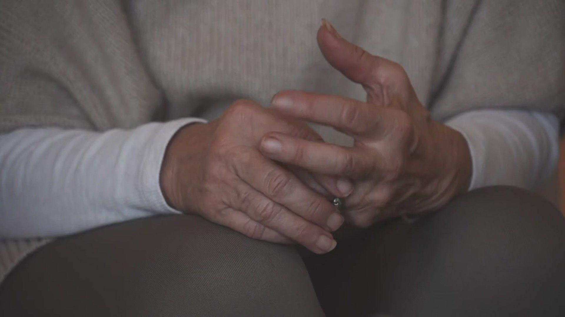 A pair of woman's hands clasped together above her knees with her face out of shot. 