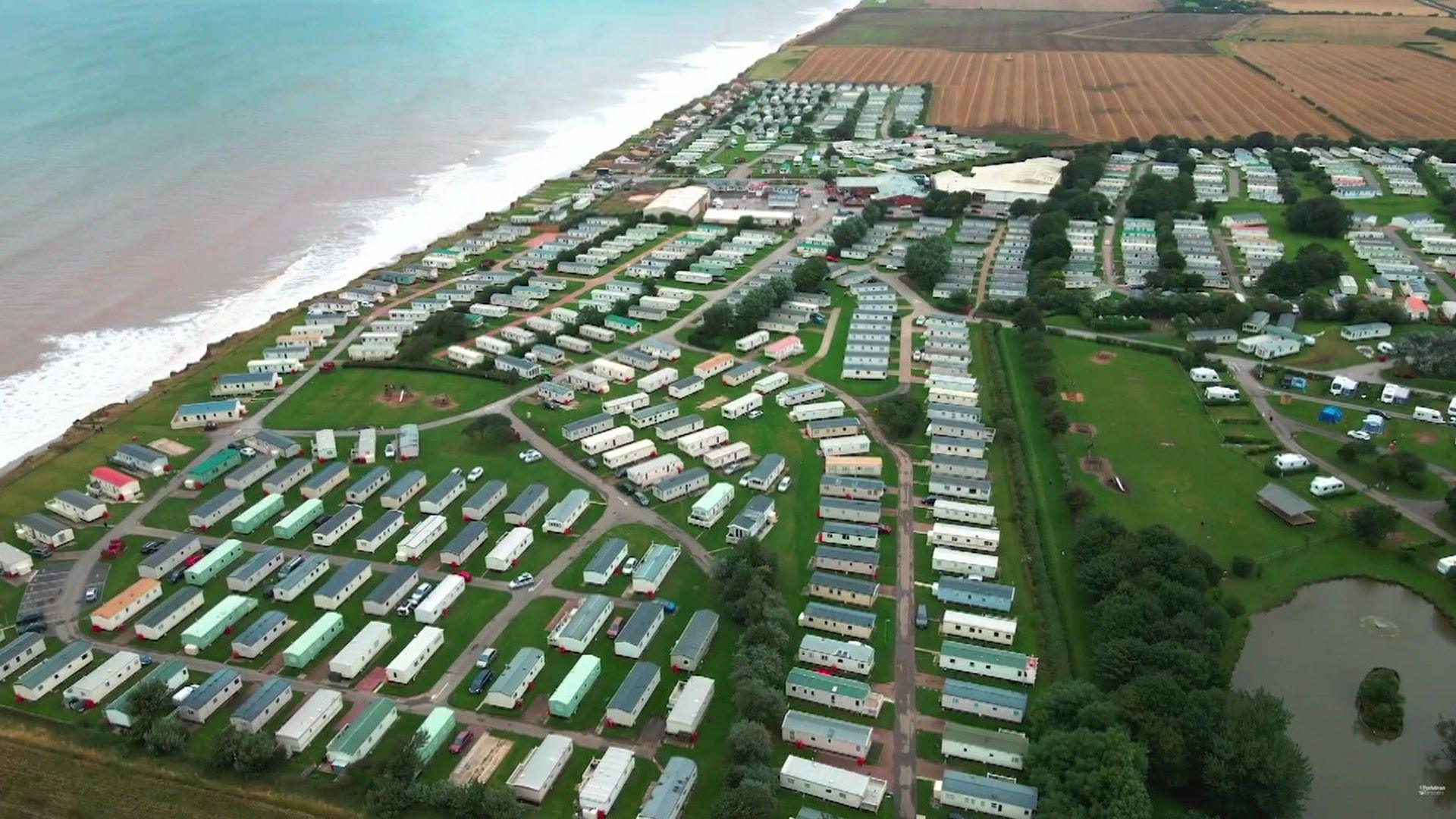 An aerial view of Skipsea Sands holiday park in East Yorkshire, with dozens of colourful caravans arranged in rows close to a beach and the sea. To the right is a large green space and a lake.