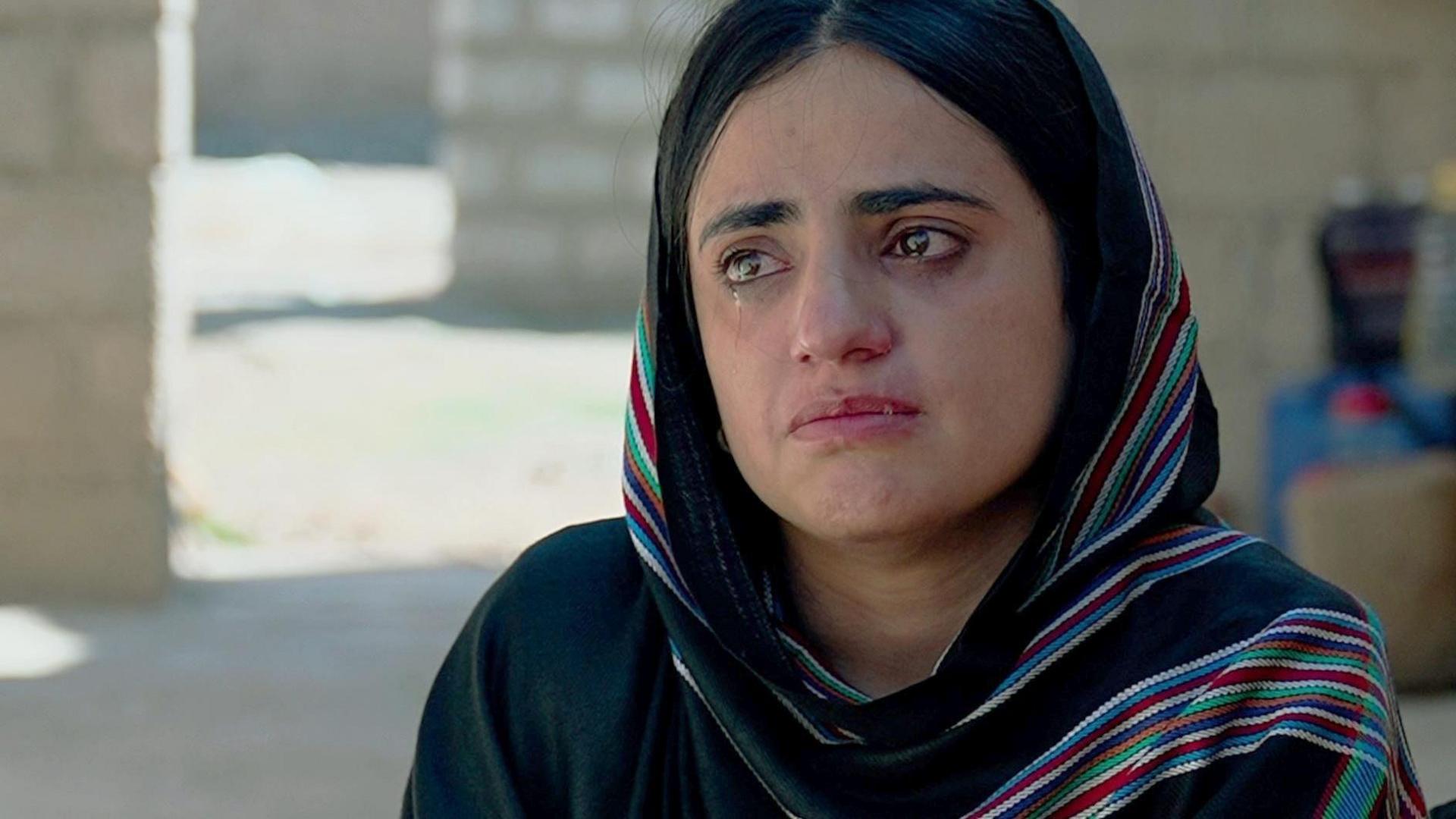 A woman in headscarf, Mahrang Baloch, looks at the camera as she cries 
