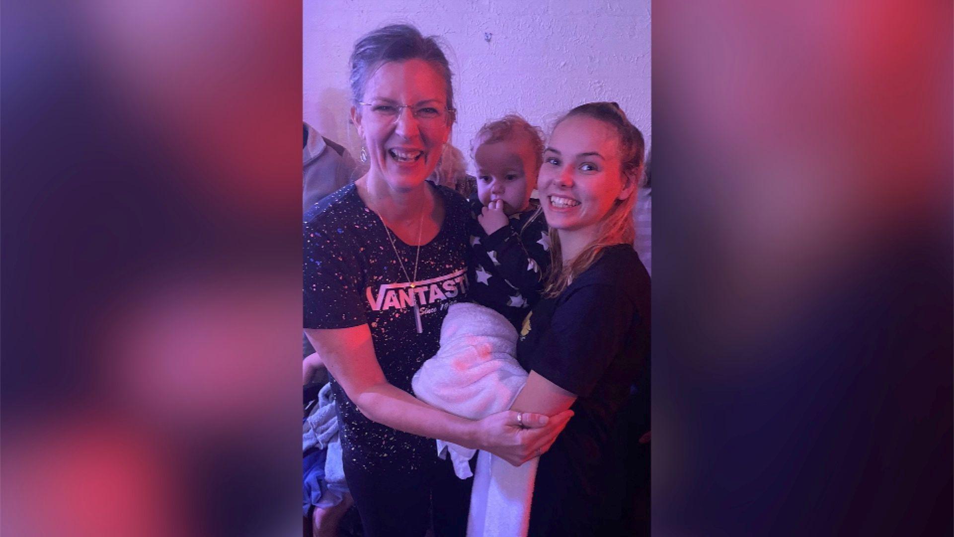 Fru and Lydia are standing either side of baby Casper and grinning widely. Lydia has long blonde hair tied up in a ponytail and wears a black cotton short sleeved t shirt. She is holding onto Casper in the middle, who wears a long sleeve black jumper with white stars on it and has short blonde curly hair. Fru is smiling and has her hair tied back and wears frameless glasses and a black cotton t shirt speckled with paint splats and reads 'Vantastic' along the front.