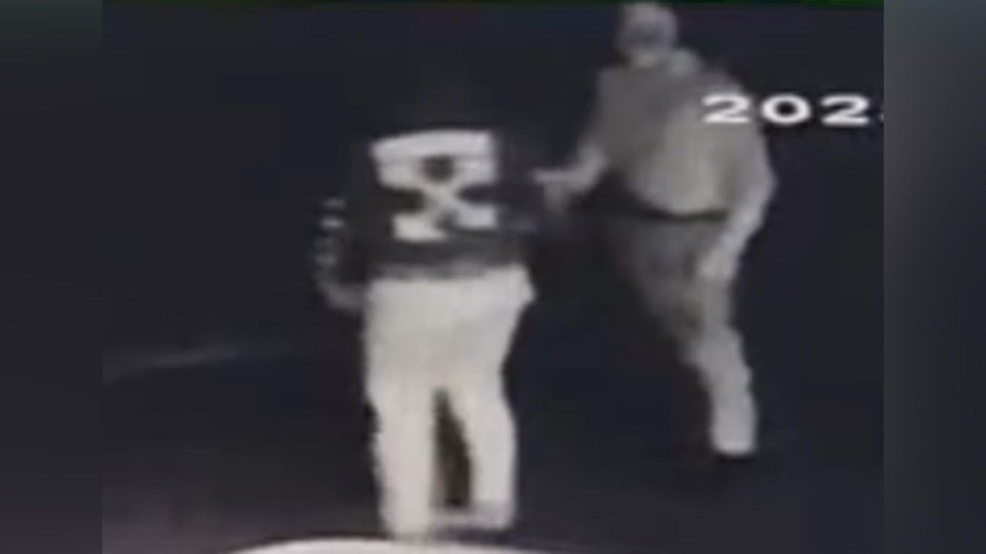 A grainy black and white still from a CCTV camera showing two figures in hoodies and trousers. The number 202 is visible in the photo from the CCTV footage.