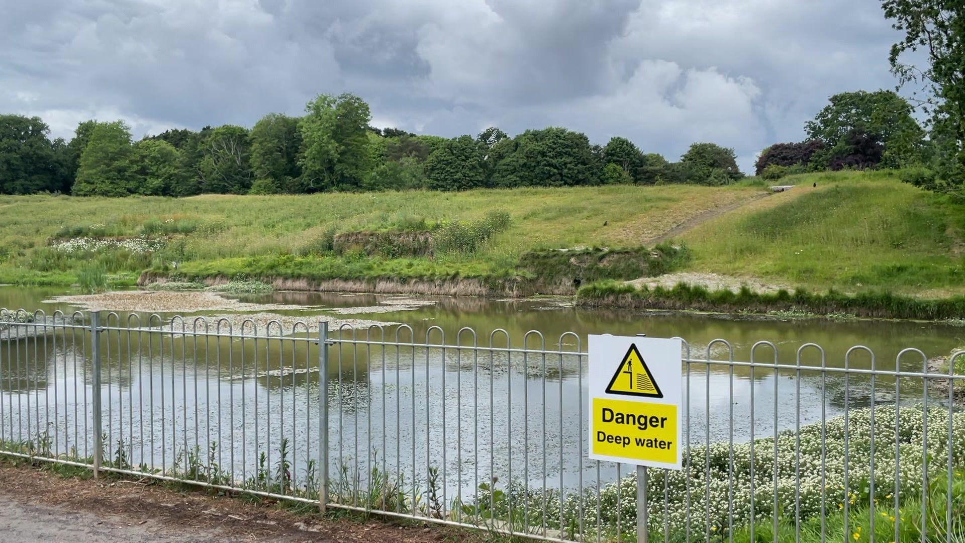 A pond with a grass bank and a sign saying Danger.