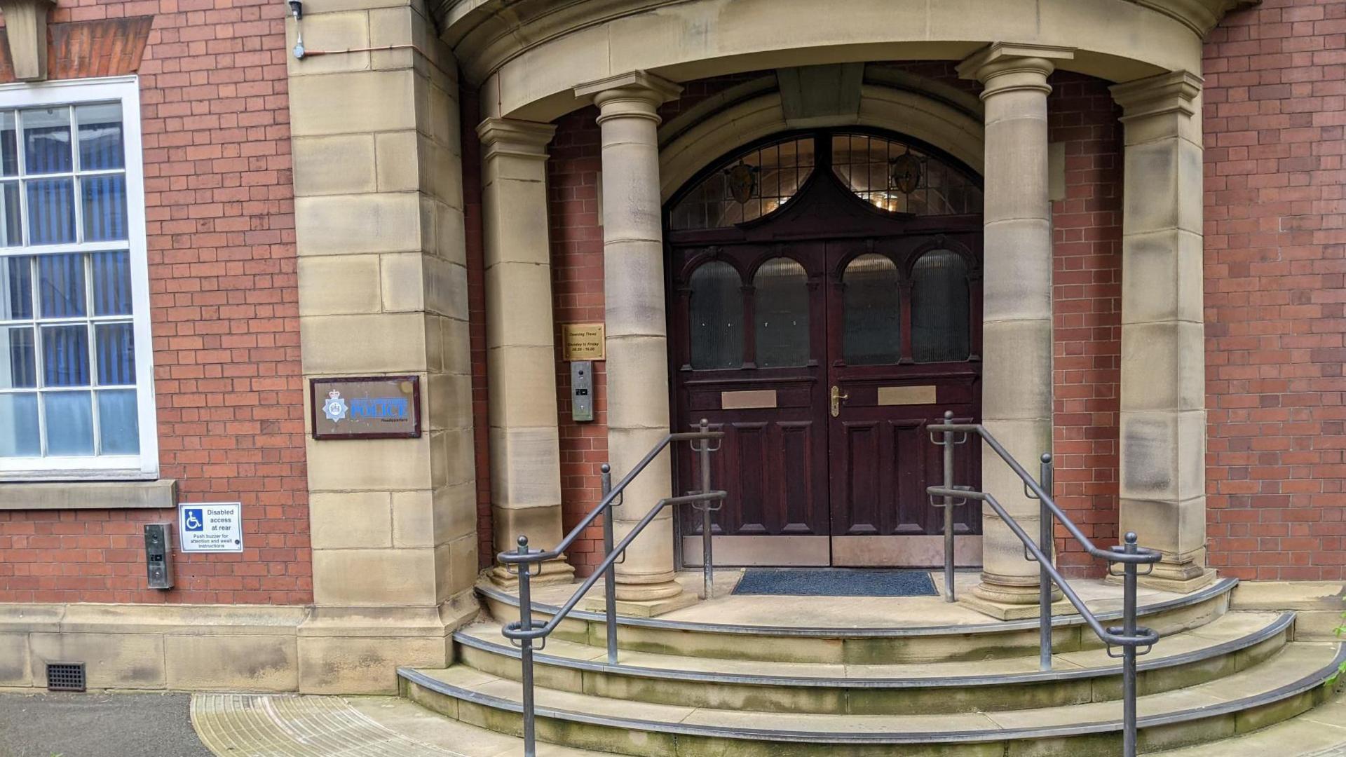 West Yorkshire Police HQ in Wakefield. Pictured is a set of oak-coloured double doors between two Roman style pillars. The police logo features to the left of the doors