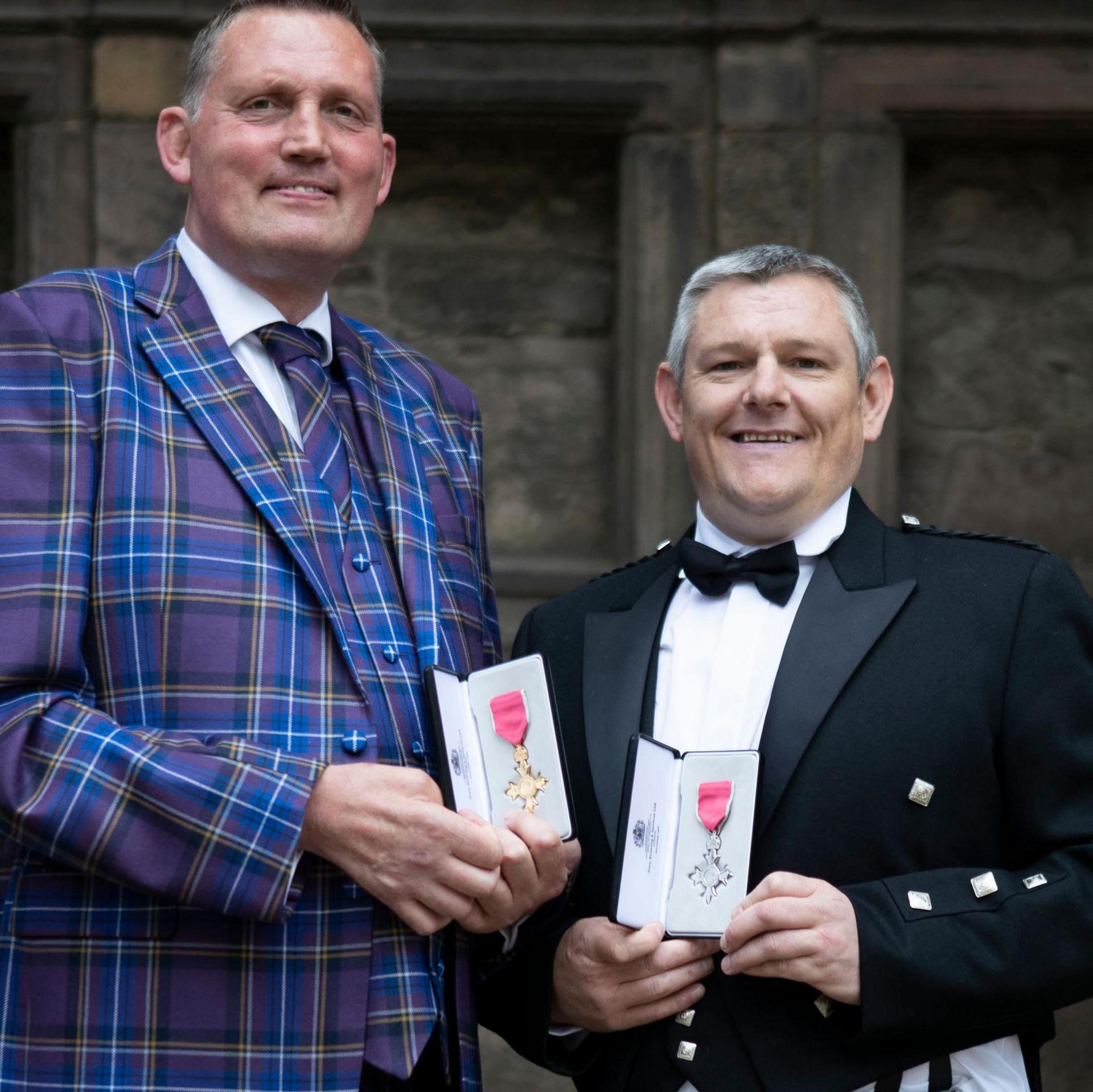 A photo of John and Doddie with their MBEs outside the palace