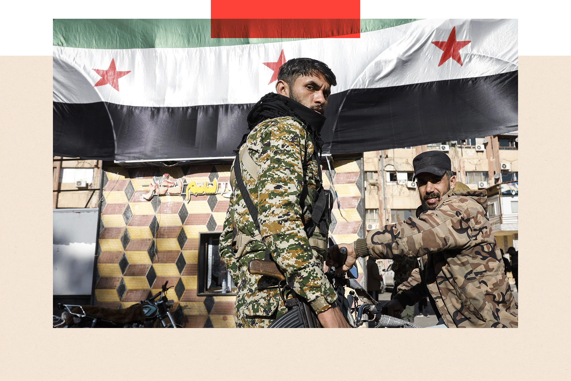 Two soldiers pose for the camera with the Syrian flag in the background