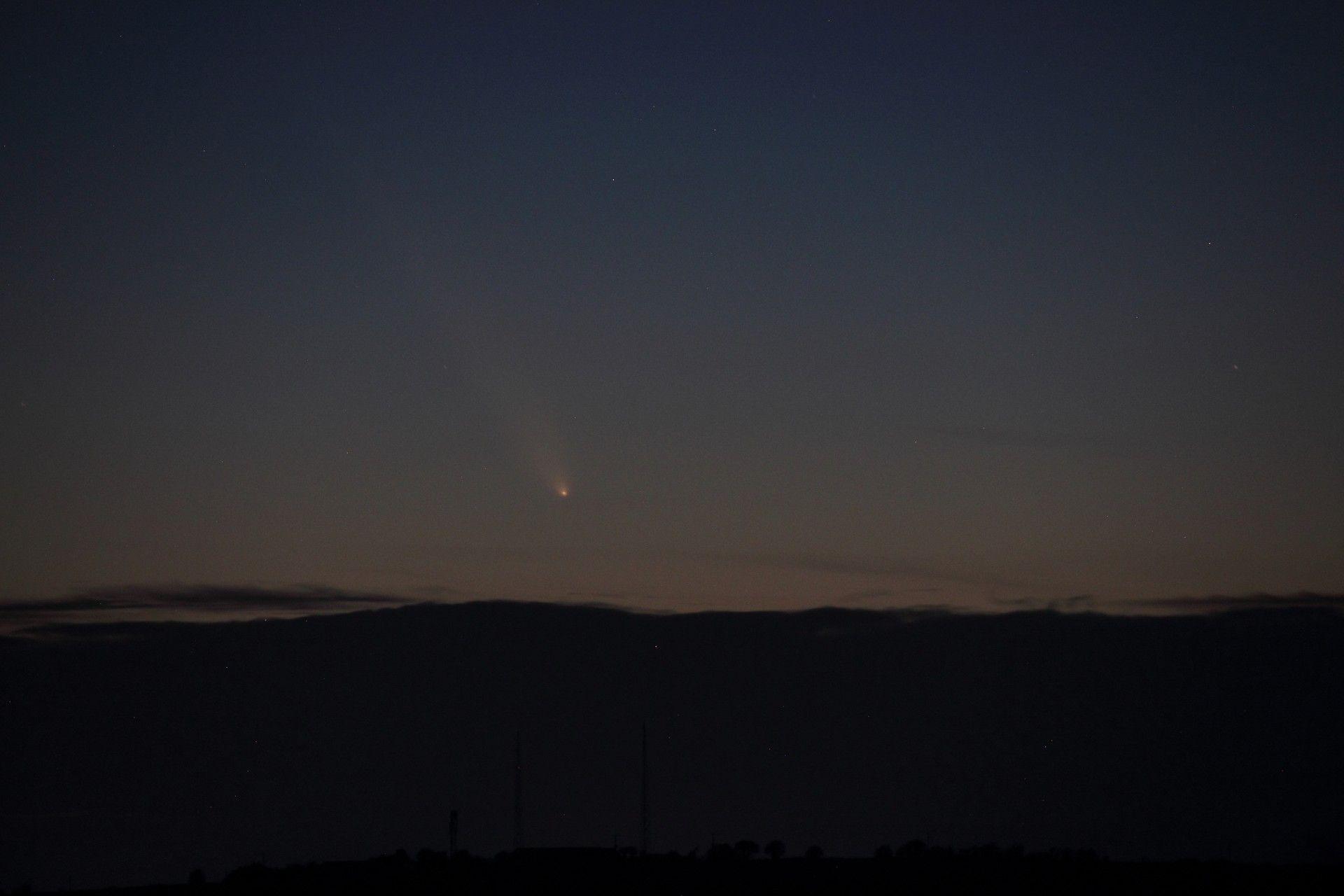 A long-distance shot of a dark night sky from a hilltop, with a bright light streaking away from the camera.
