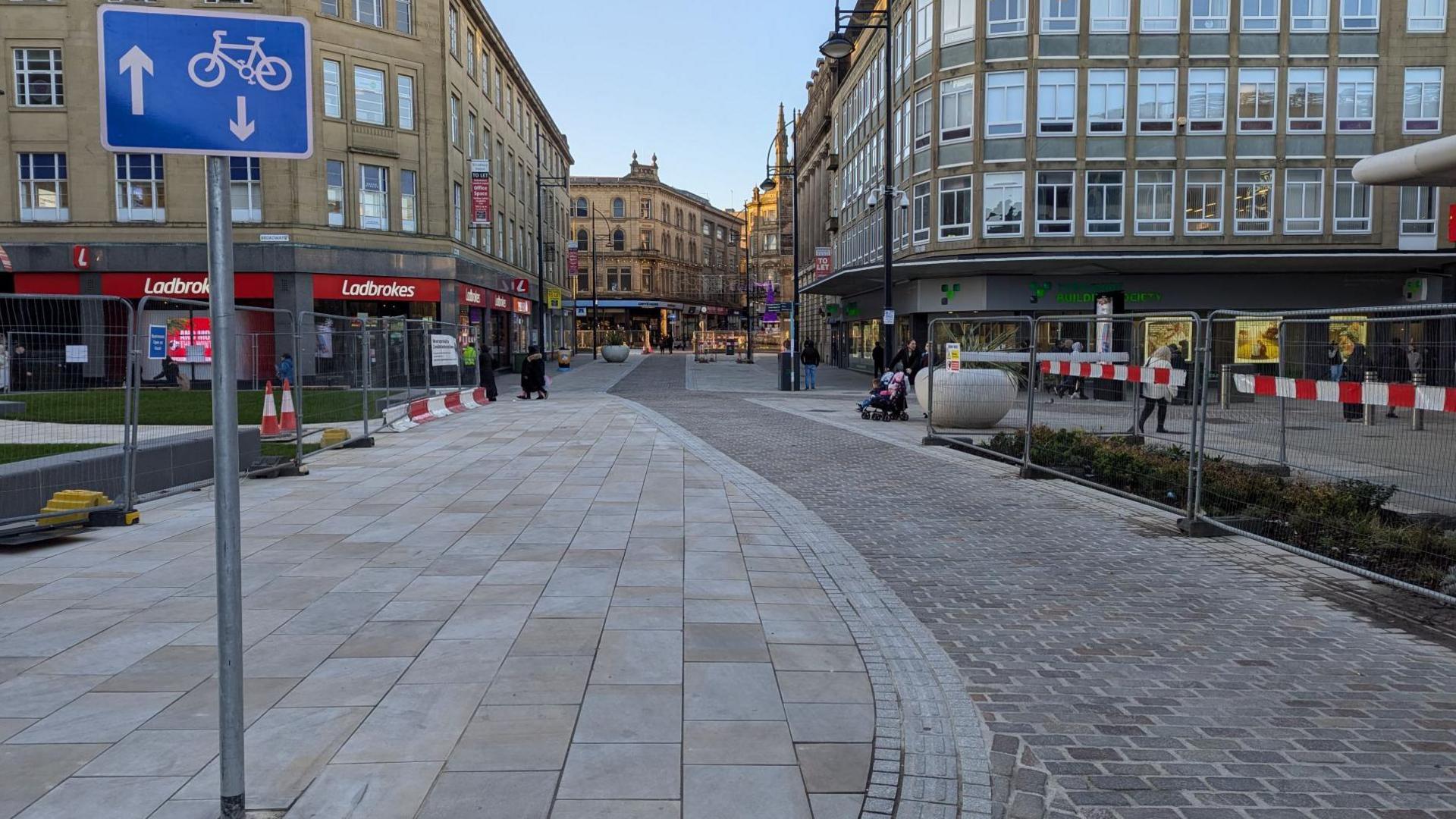 A pedestrianised road and cycle route in Bradford, there are metal fences on either side.