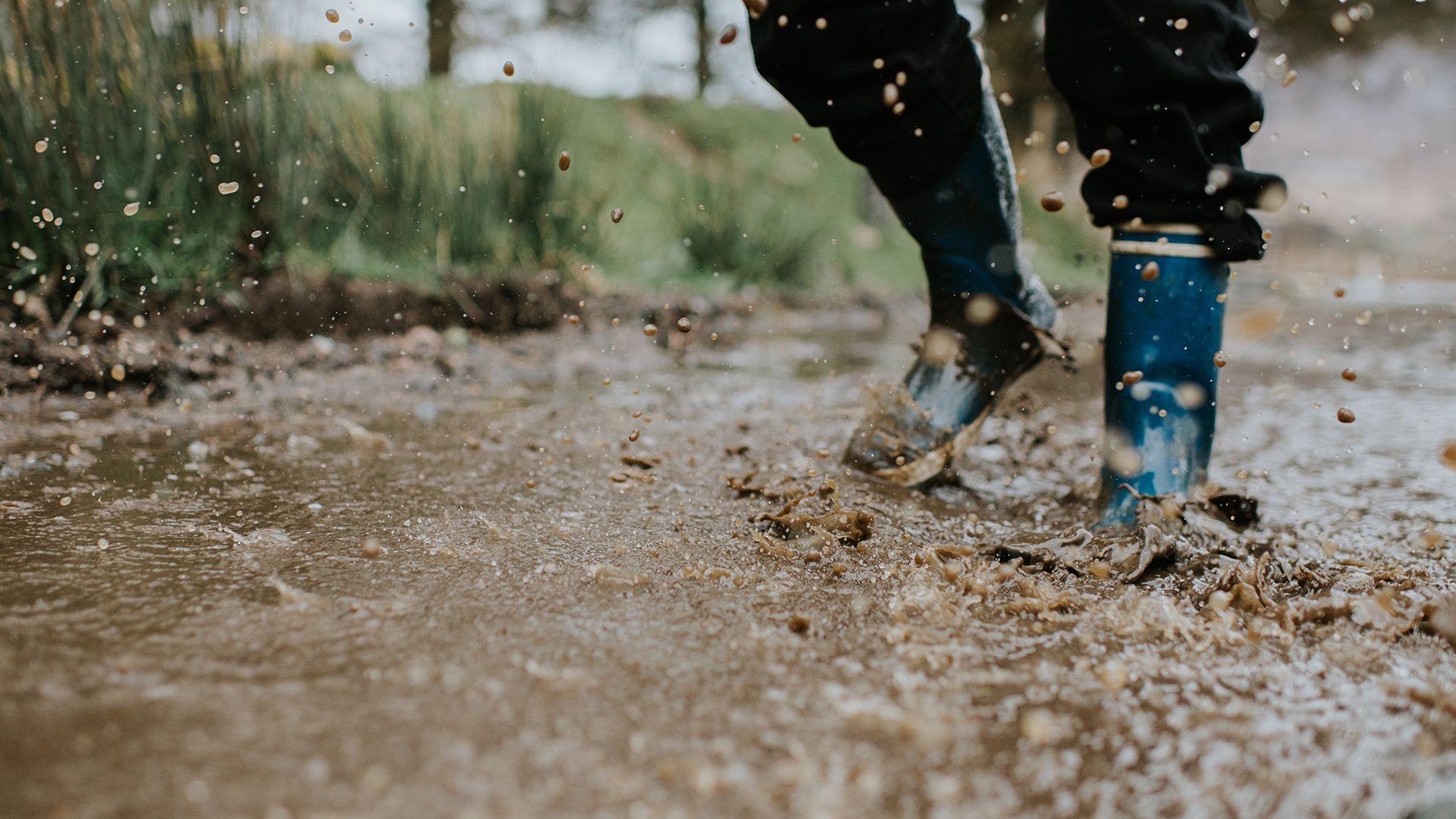 Blue wellington boots spash in a muddy puddle