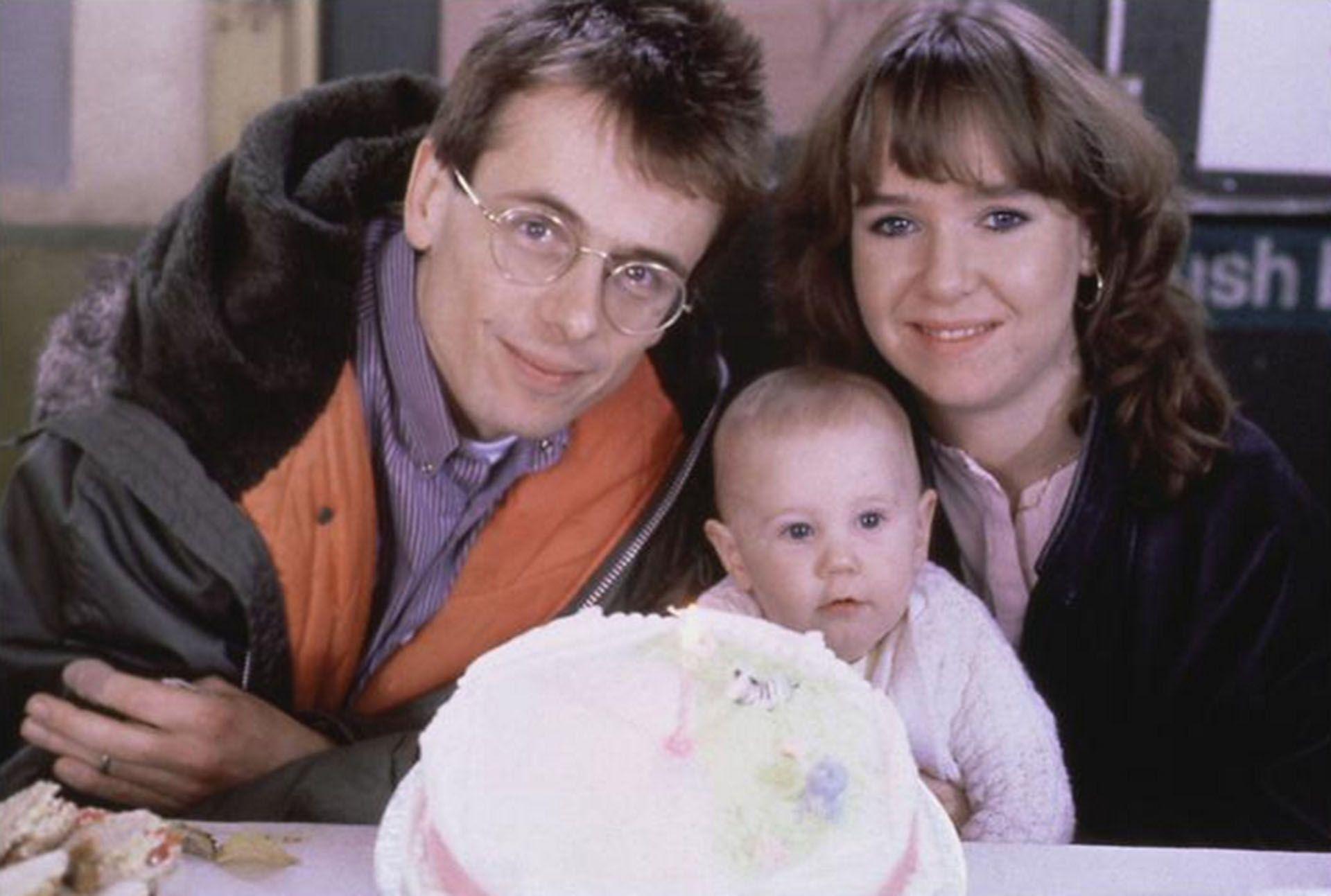 tom watt, susan tully and a baby pose next to a childs birthday cake