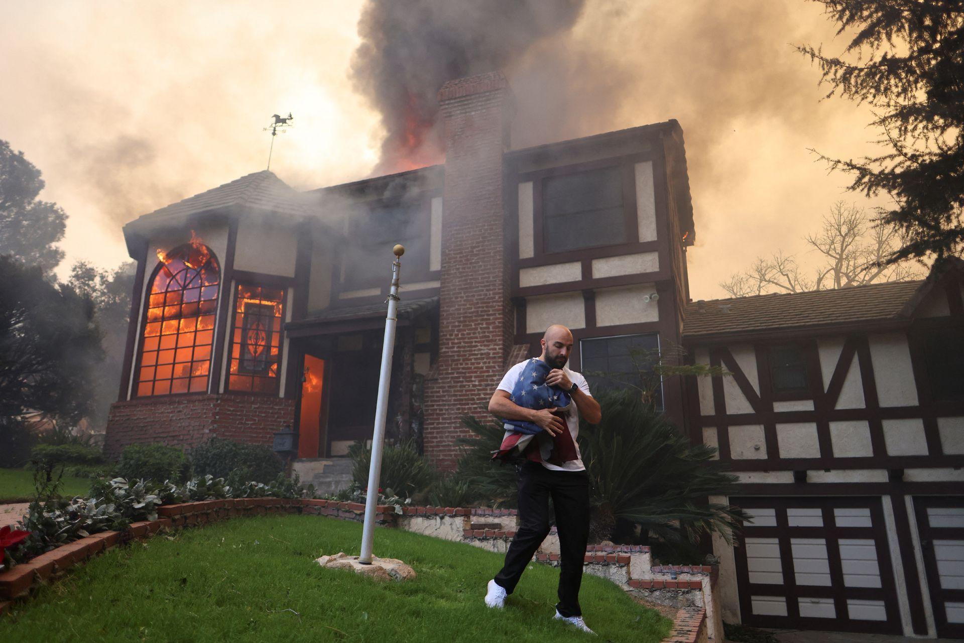 A person carrying a US flag after removing it from the flagpole in their garden walks away from a burning house at the Eaton Fire in Altadena on Wednesday.