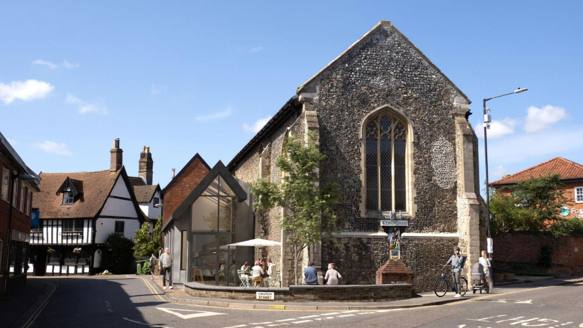 An image of Becket's Chapel in Wymondham, Norfolk. The stone building has arched windows and an arched roof. There are properties either side with a road in front.