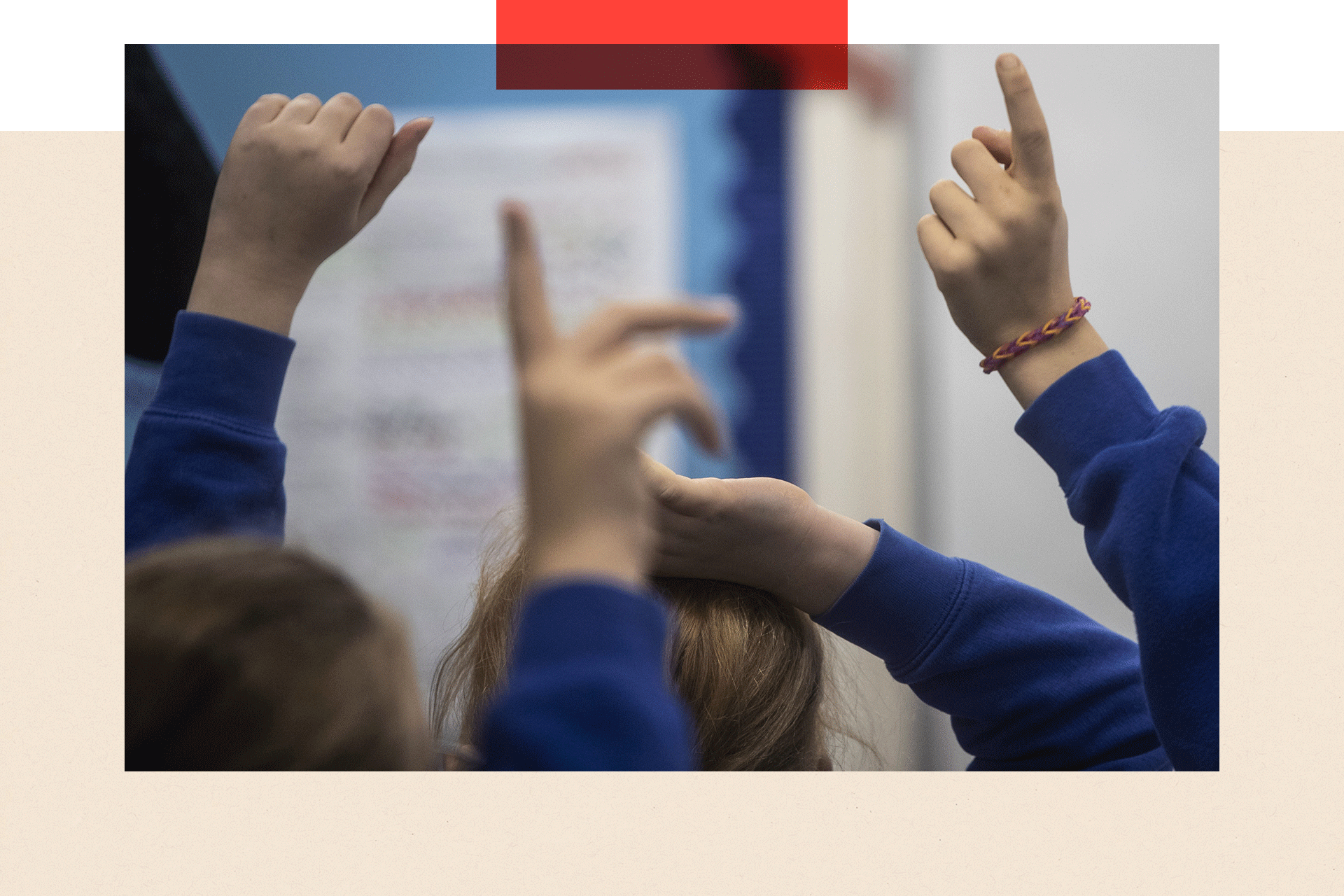 School children in a classroom raise their hands up