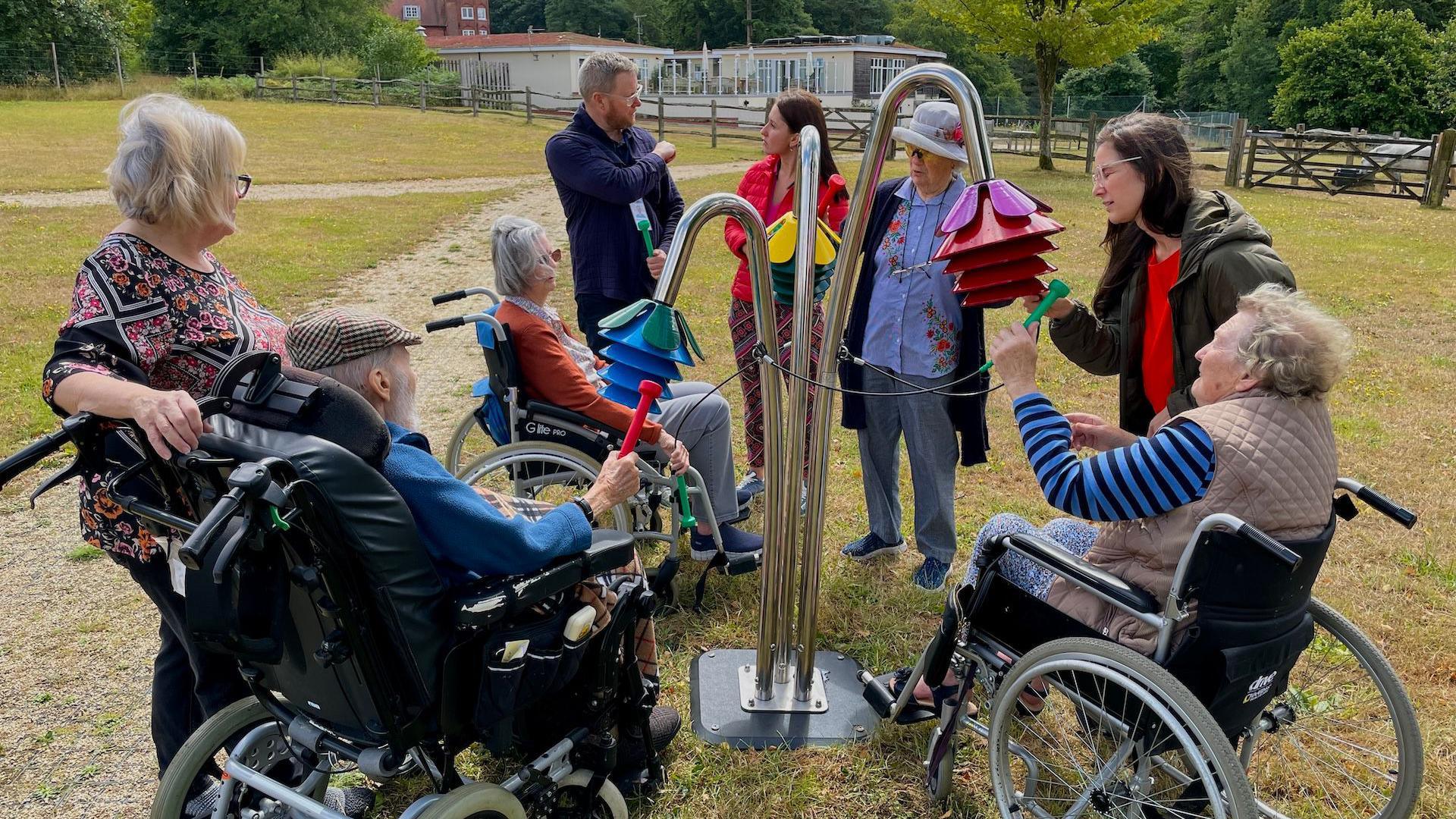 A group of residents play tubular bells in a garden, some in wheelchairs