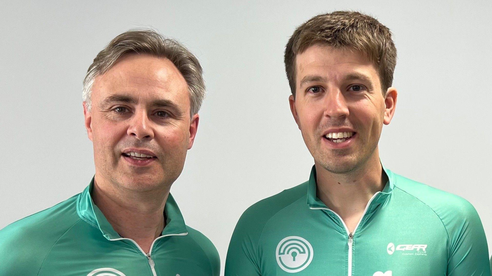 Two men, smiling. They are wearing matching mint green cyclist tops.