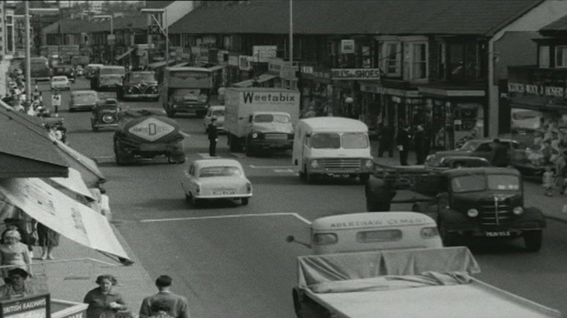 Llun du a gwyn o'r hen A49 drwy Port Talbot, yn dyddio o'r cyfnod cyn adeiladu'r ffordd osgoi. Mae nifer fawr o geir gan gynnwys lorïau o bob math a maint, i'w gweld yn teithio'n araf mewn ardal brysur llawn siopau