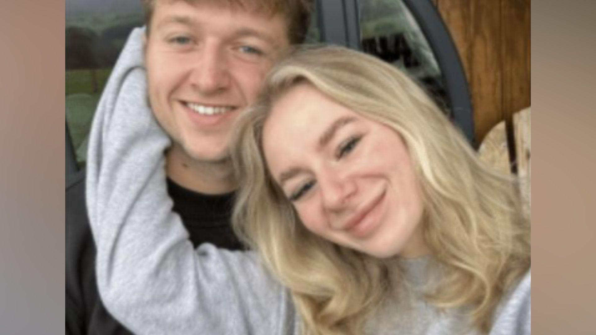 Sam Littler, in his 20s, who has dark blonde hair and a black t-shirt, smiles at the camera. Lucy Harrison, 23, who has wavy blonde hair and a grey sweatshirt, rests her head agains his cheek and holds her right hand to his face affectionately. 