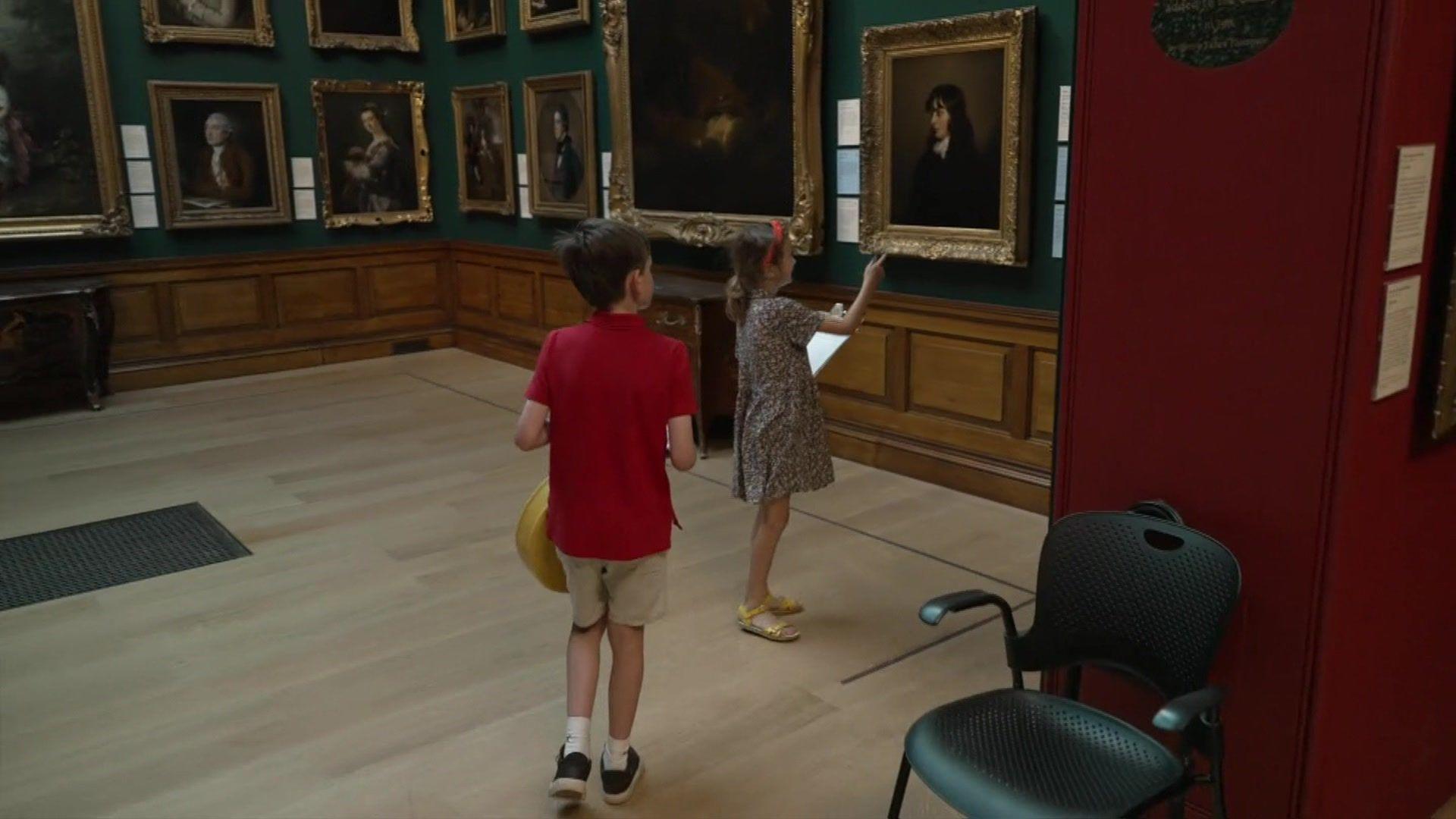 A boy and a girl walking through an art gallery - the girl is pointing to one of the portraits