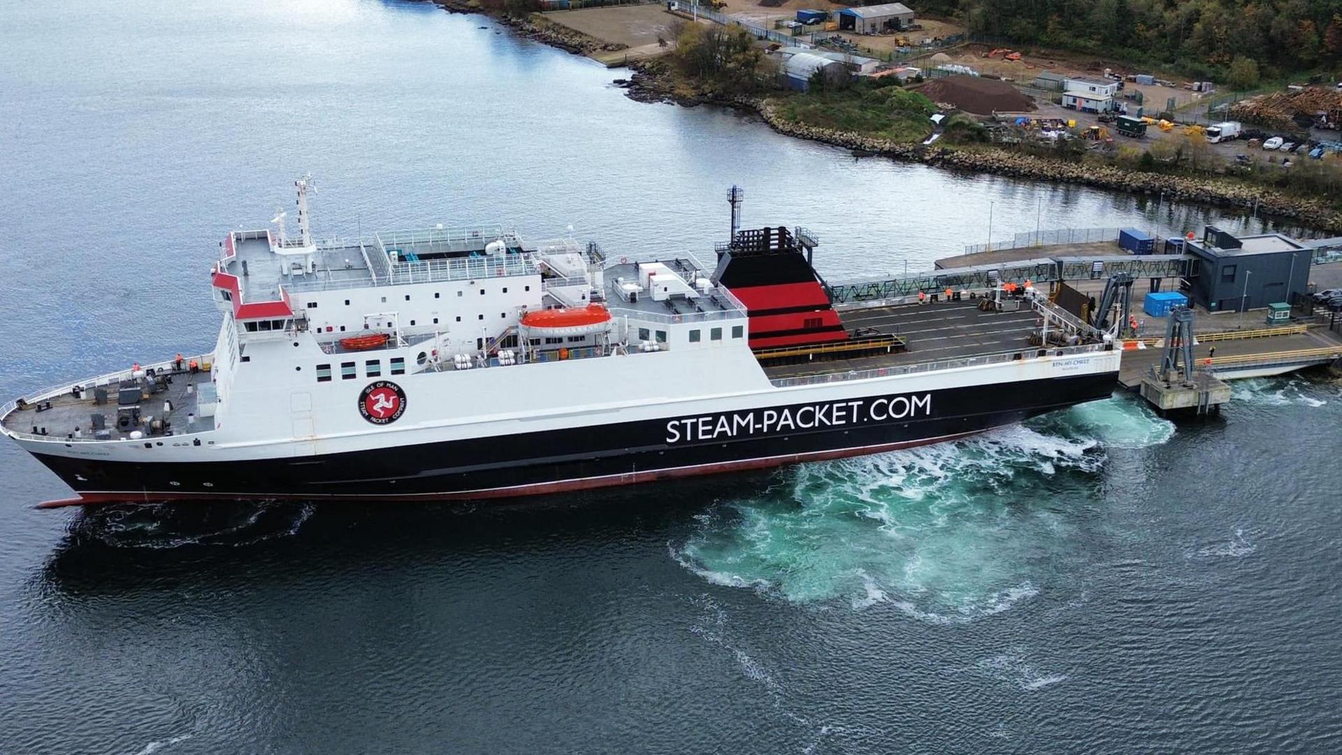 A black and white ship with a red funnel, viewed side on, reversing towards the berth at Brodick