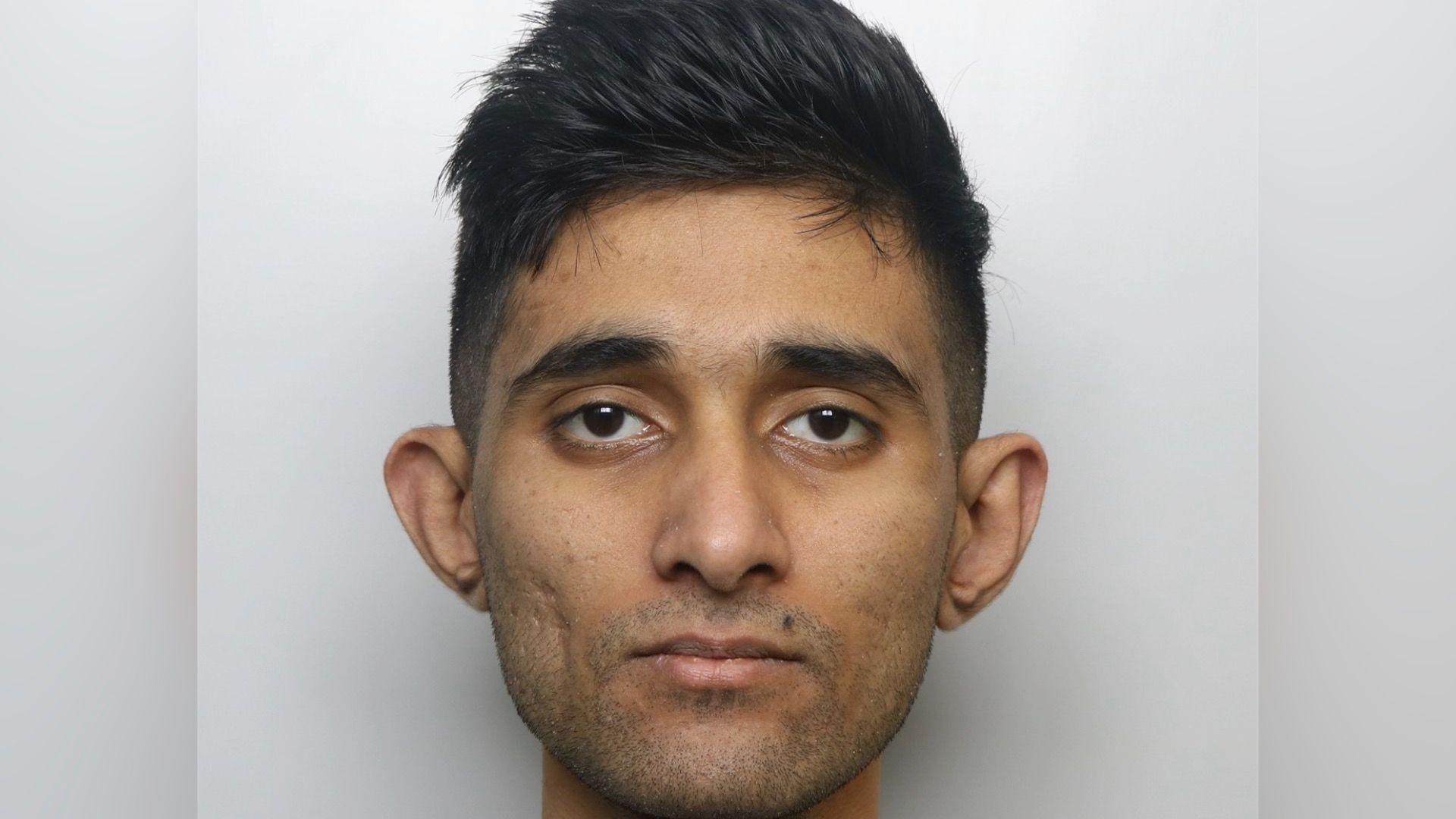 Man without a beard with dark hair cut short at the sides and slightly longer and ruffled up on top - a police mugshot picture