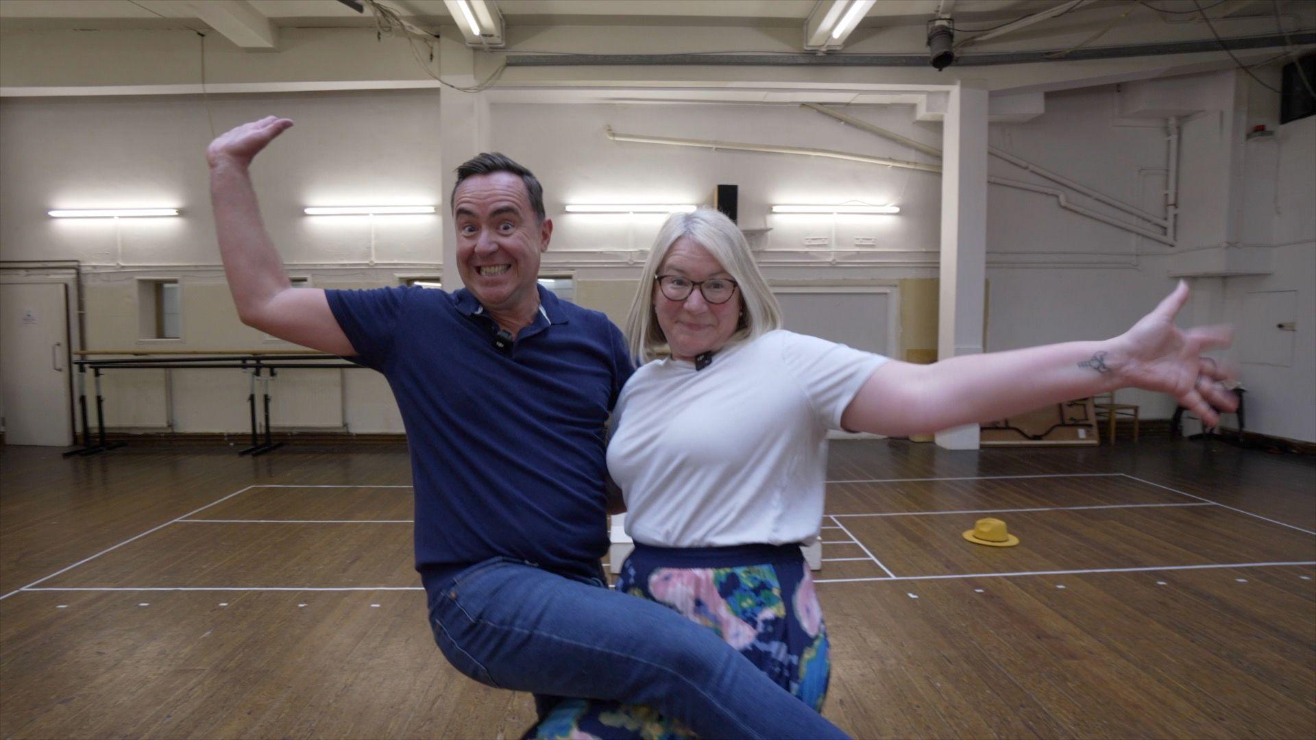 Edward Sault and Sophie Law are dancing with their arms outstretched and leg over one another.