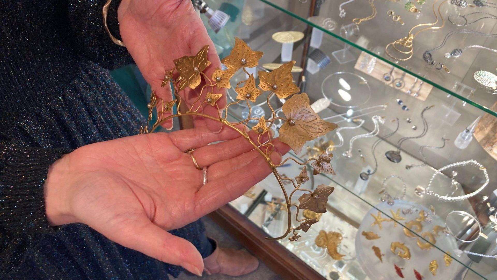 A gold coloured tiara with ivy leaf design being held in someone's hands.