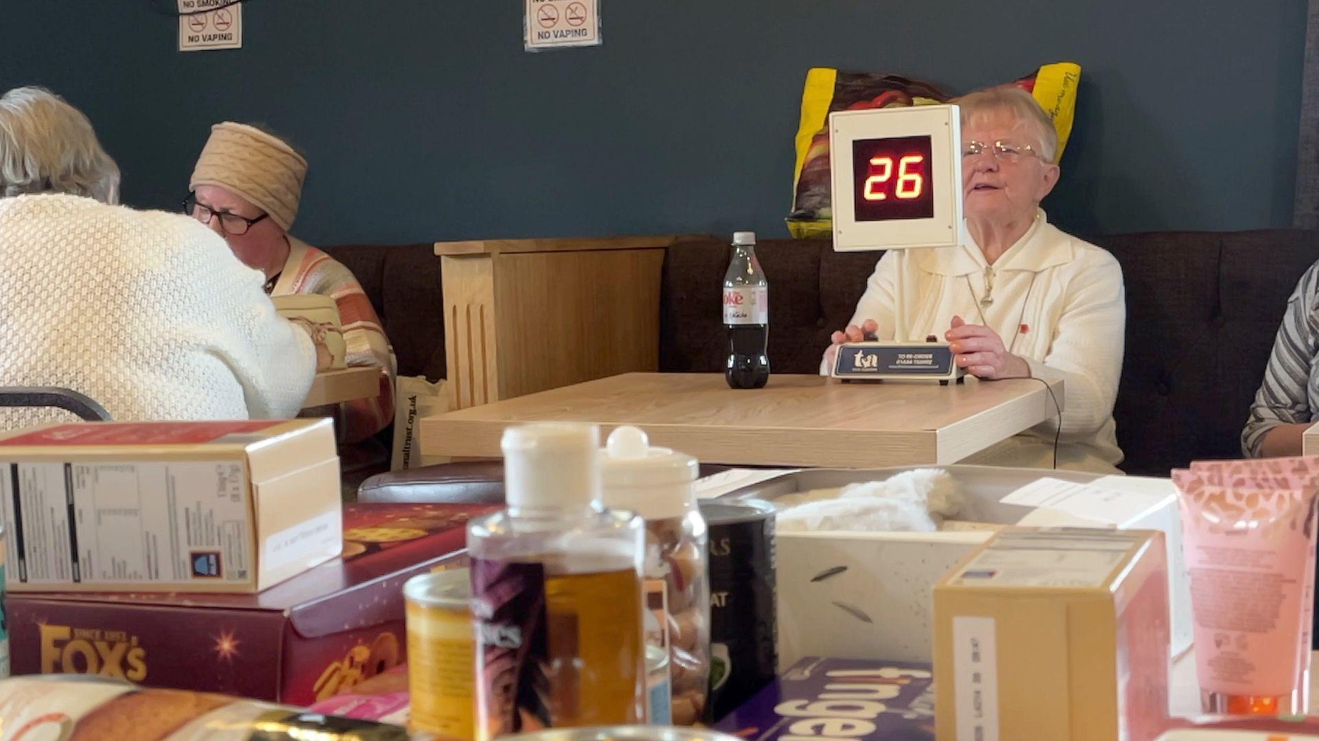 A club member calling bingo numbers with prizes in the foreground