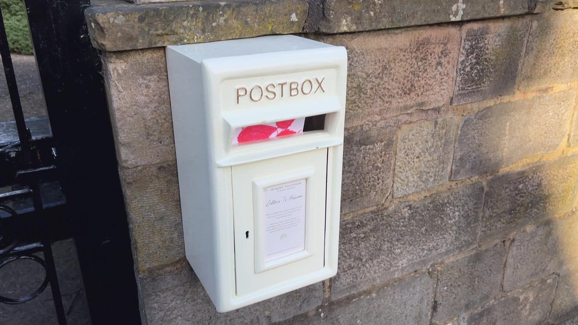 The "letters to heaven" post-box coloured white mounted on a brick wall.