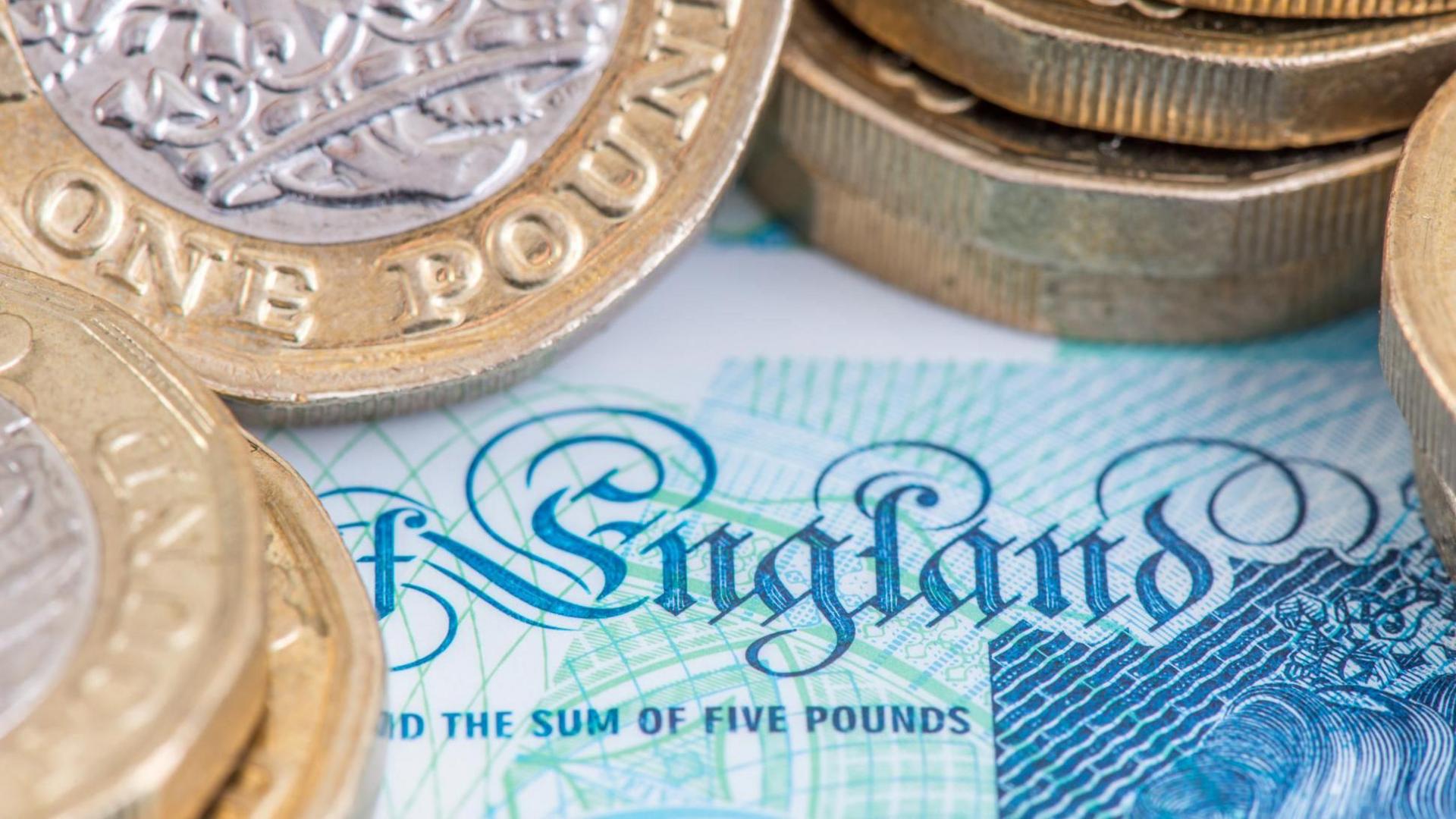 Several £1 coins are stacked on top of a £5 note. 