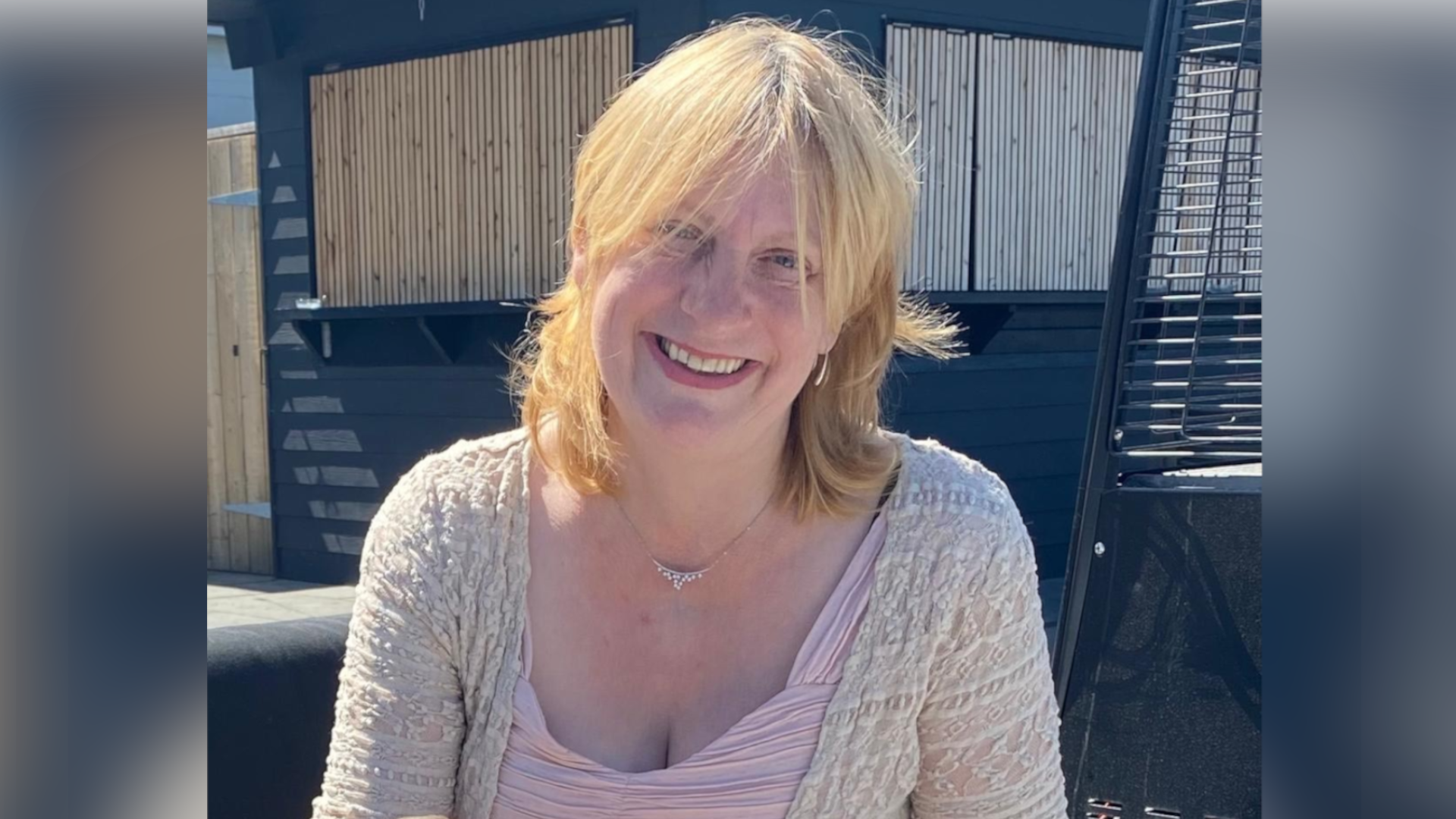 Rosie Wilson, a woman who is sitting down outside with blonde hair. She is wearing a pink T-shirt and grey cardigan and is looking directly at the camera and smiling.