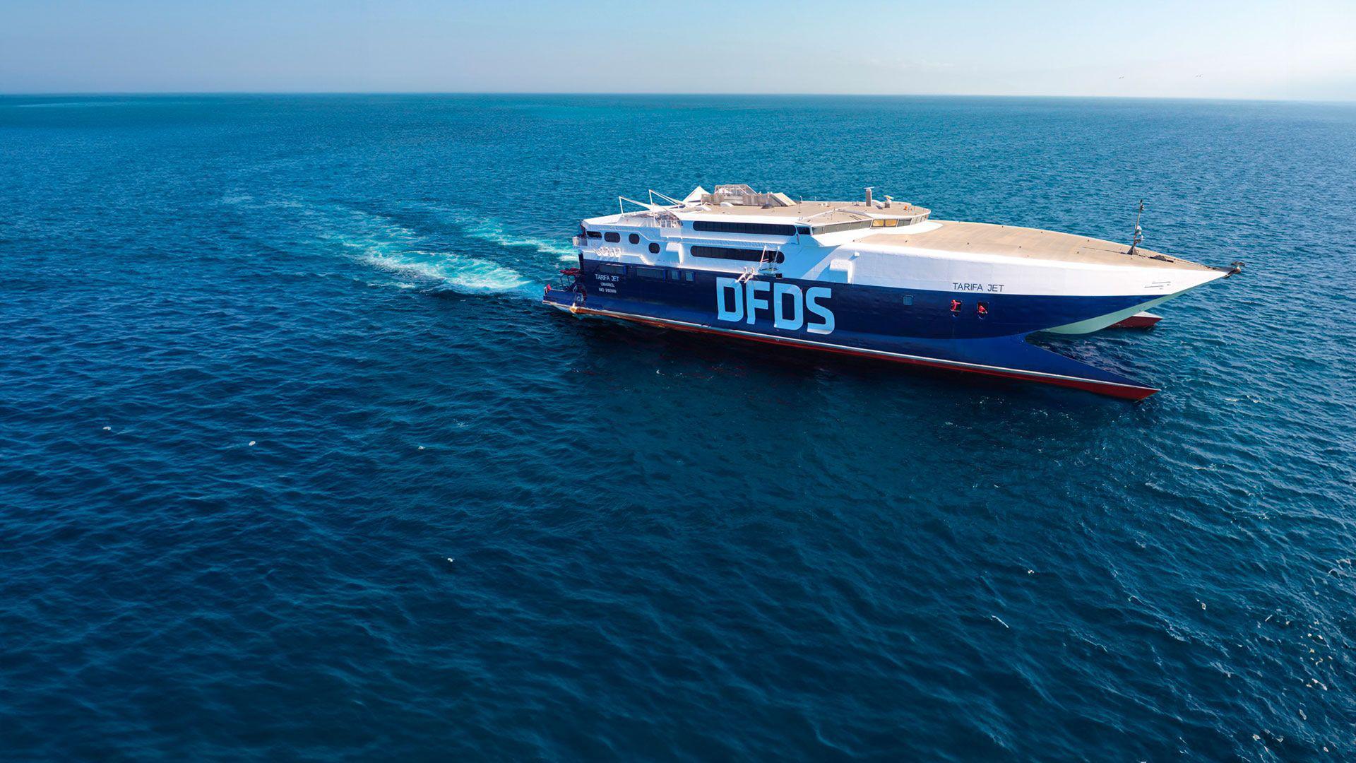 A blue, red, and white ferry in the sea. There are the letters 'DFDS' on the side of the ferry, and the words 'Tarifa Jet' in smaller text. 