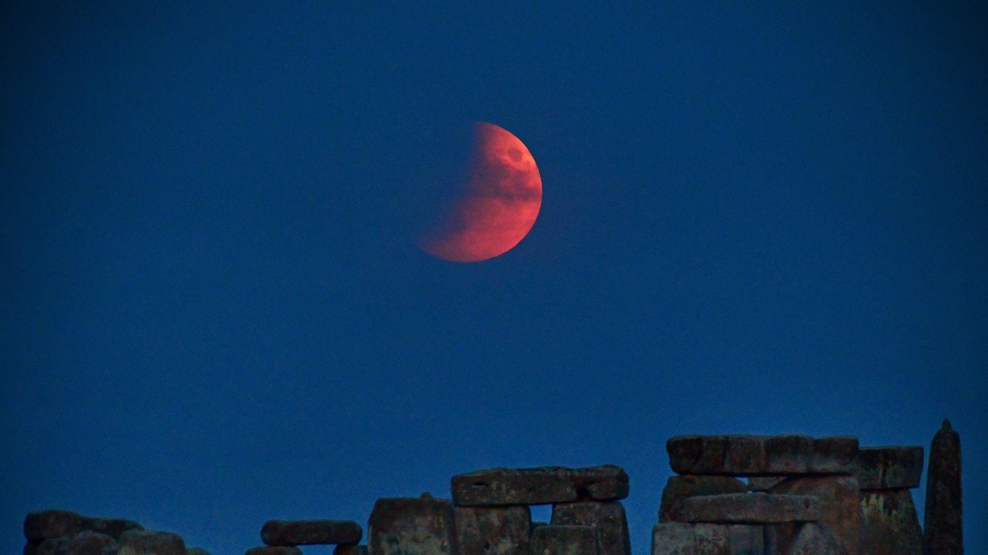 Red crescent moon above Stonehenge illuminating the night sky