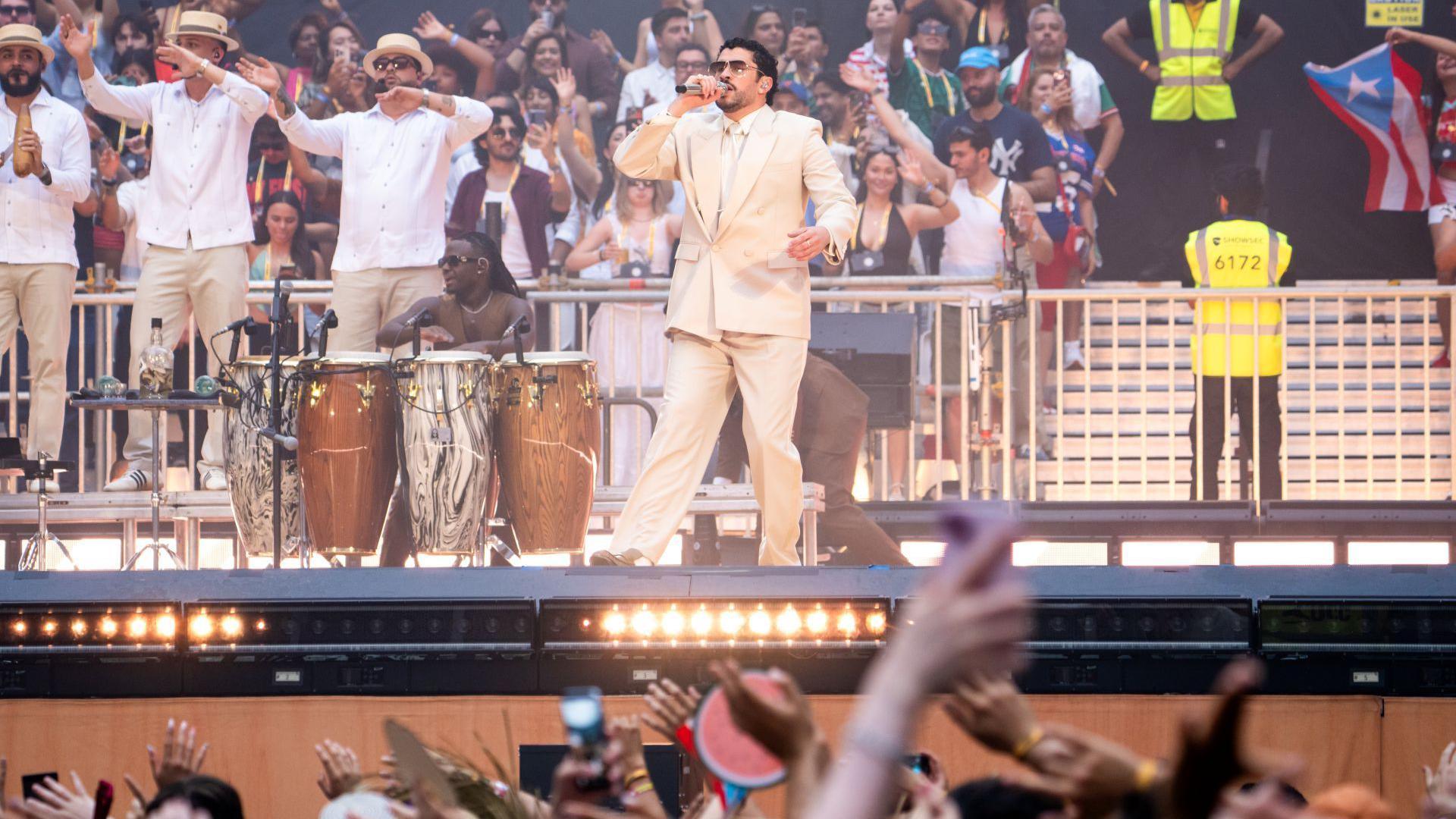 Bad Bunny on stage with musicians as members of the crowd behind him and in front of him watch and wave their hands