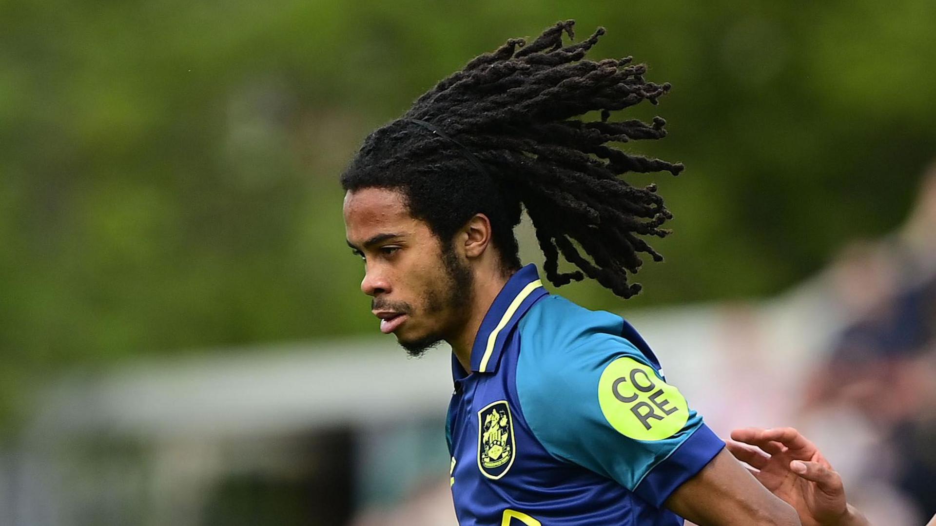 Neo Eccleston playing for Huddersfield Town in their away kit of blue with lime trim