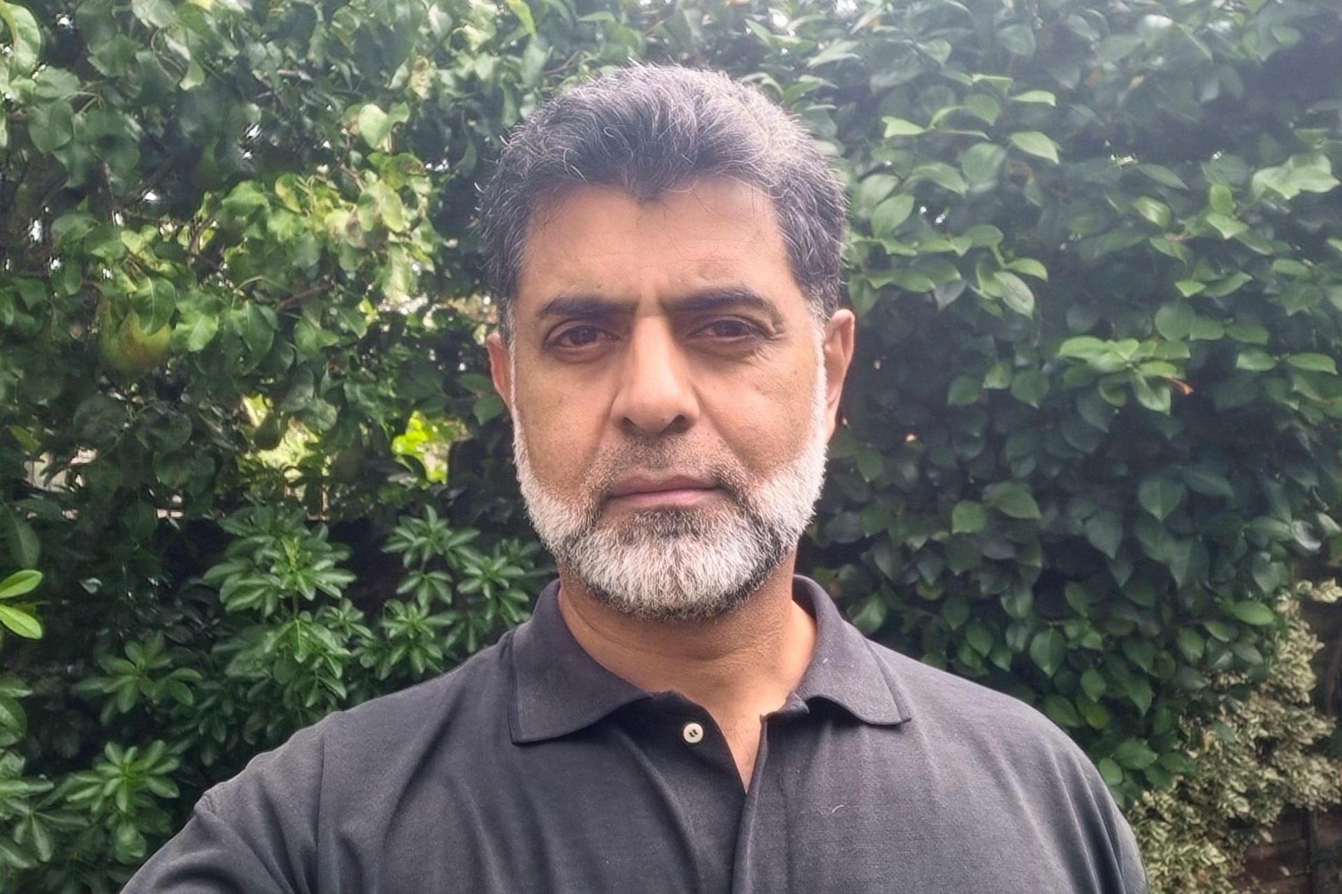 Sohale Rahman standing outside in front of a bush, with a black top on