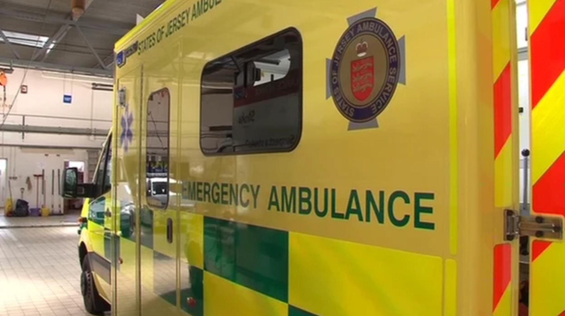 The side of a Jersey ambulance. It is mainly yellow with some green and text reading States of Jersey Ambulance and Emergency Ambulance.